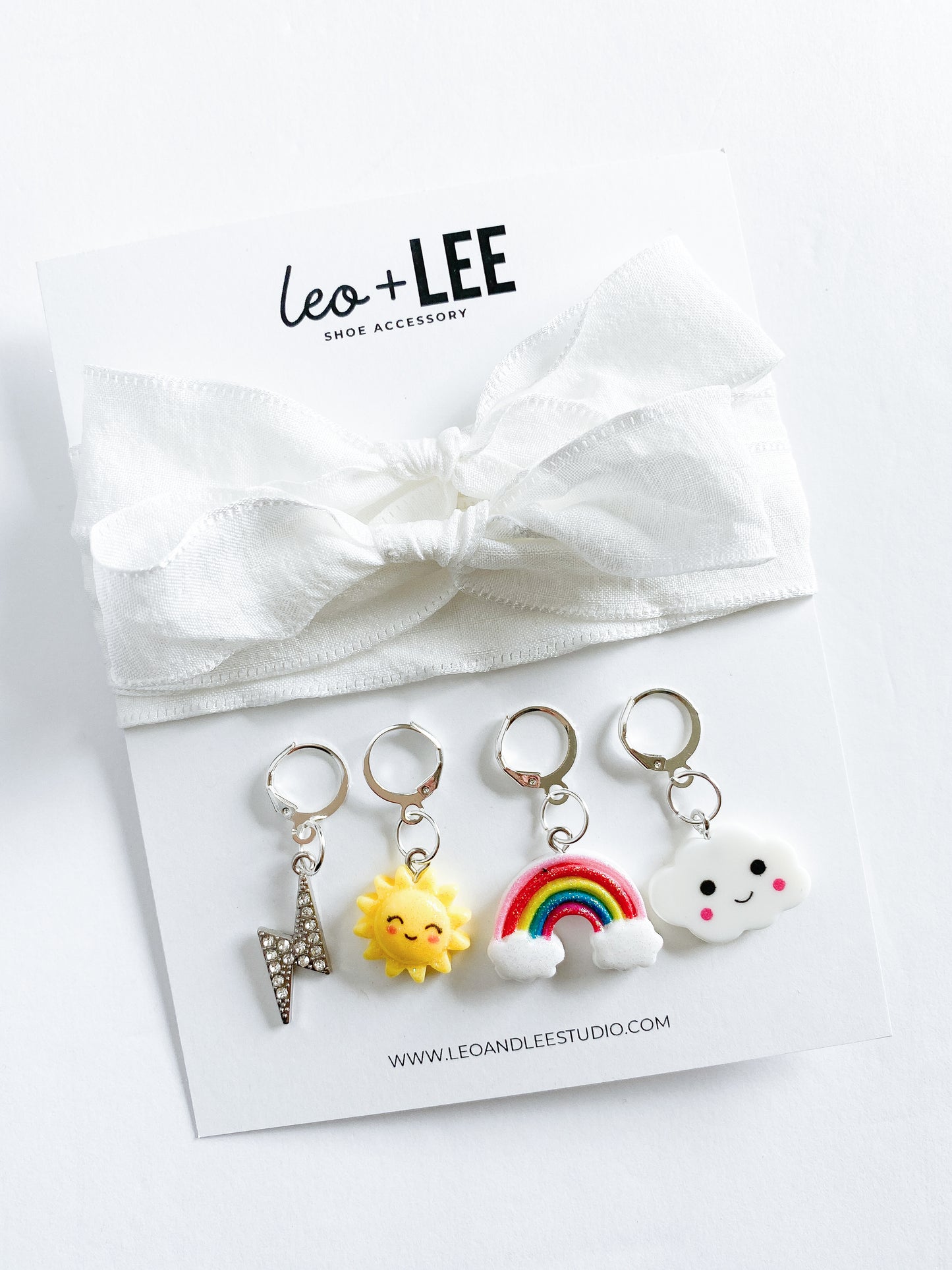 Assorted kids sneaker charm sets displayed in rows, each featuring 100cm bow-style ribbon shoelaces and four colorful enamel shoe charms on branded cards.