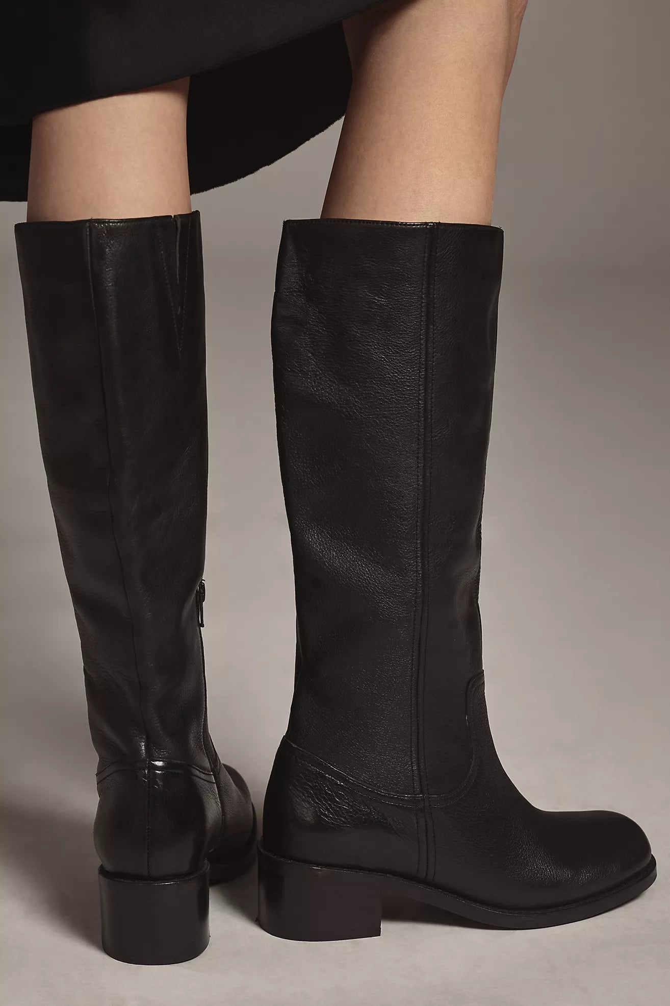 Black knee-high boots worn by a person on a neutral background
