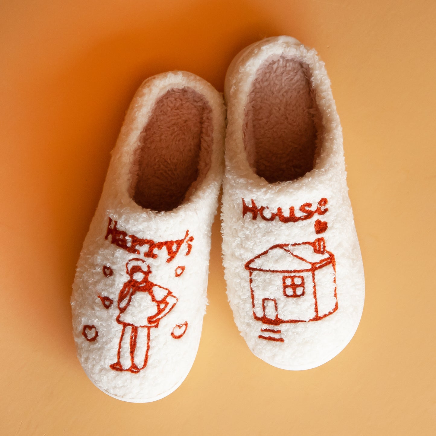Cozy white slippers featuring a charming 'Harry's House' design with hand-drawn illustrations, perfect for keeping your feet warm and comfortable indoors.