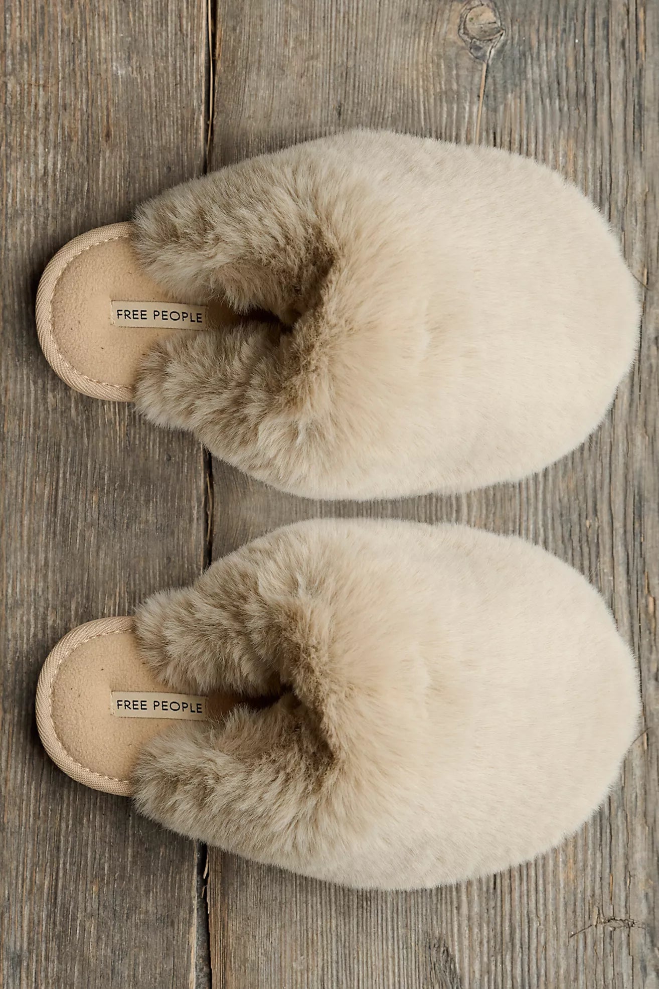 Pair of beige slippers with fur trim on a wooden surface, featuring 'Free People' branding.