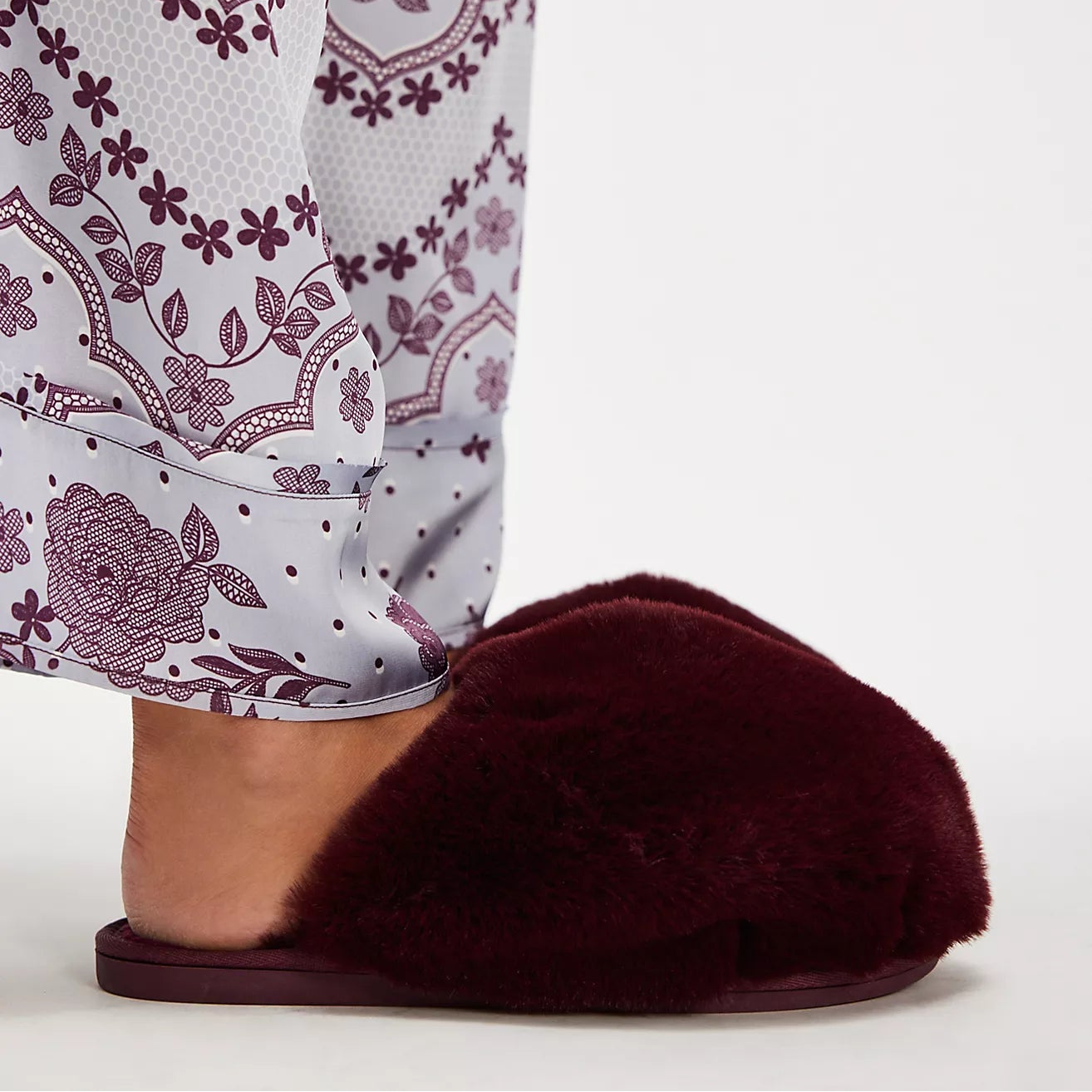 Burgundy slipper worn with floral-patterned pajama pants on a white background