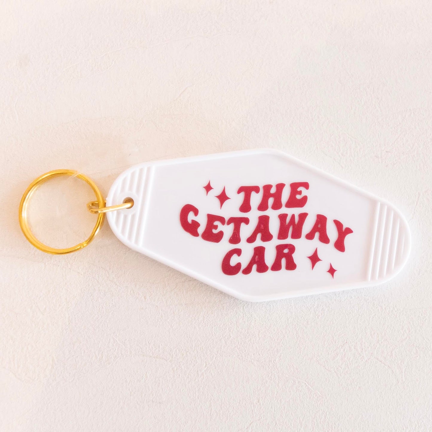 Vintage-inspired keychain with 'The Getaway Car' text and stars, made from white acrylic with a golden keyring. Perfect for adding a quirky, retro touch to your keys.