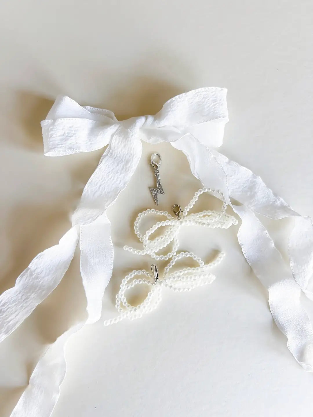 White shoe lace accessory with a lightning bolt charm and pearl bow charm on a branded card, set against a light background.