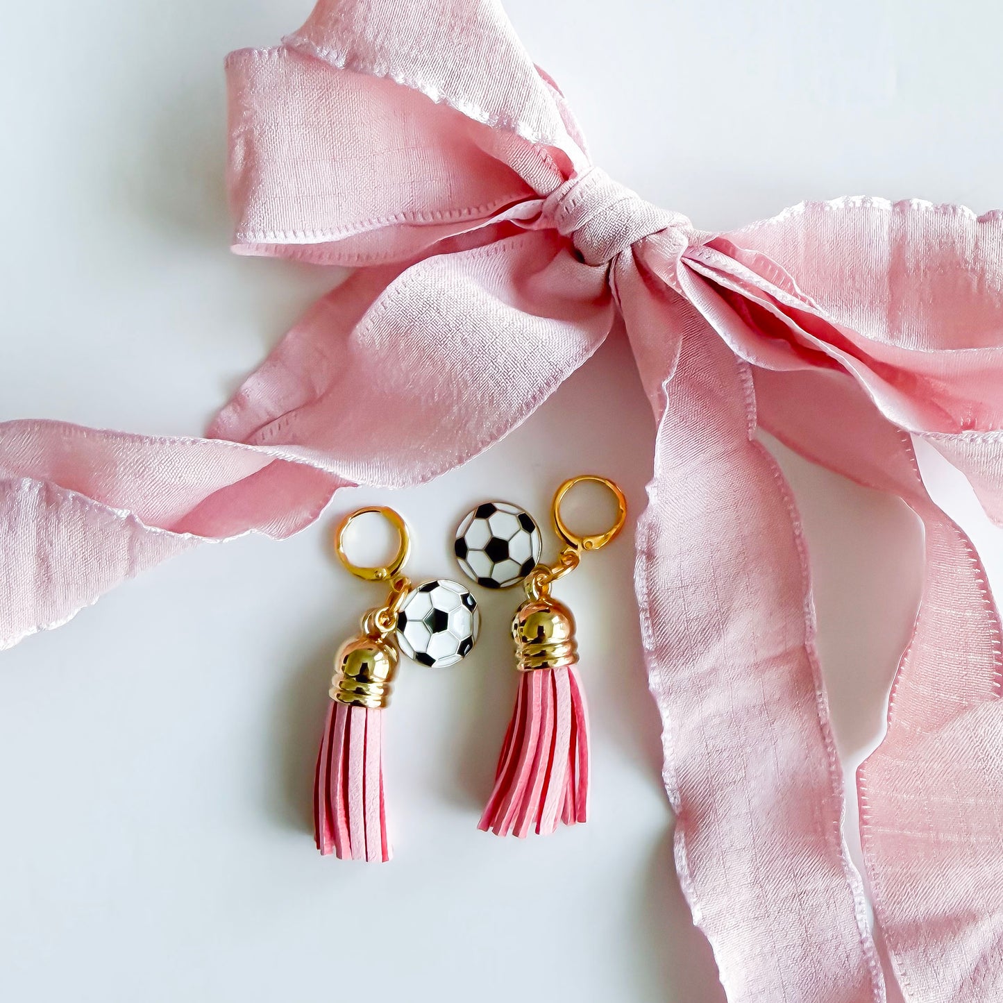 close up of Pink laces with tassels and soccer charms on a white card with brand name.