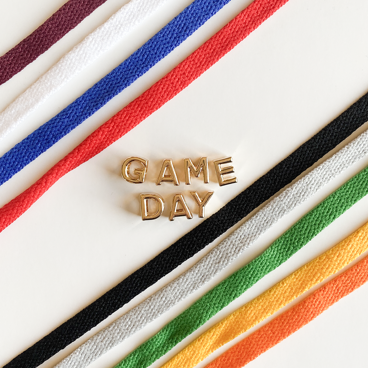 A close-up image shoelaces tied in a bow, accompanied by gold letter charms spelling "GAME DAY" displayed below.