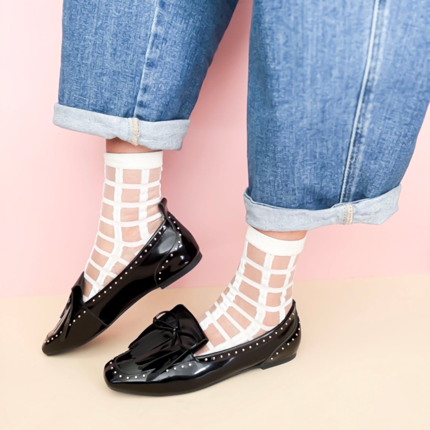 Black loafers worn with white fishnet socks and blue jeans on a pink background