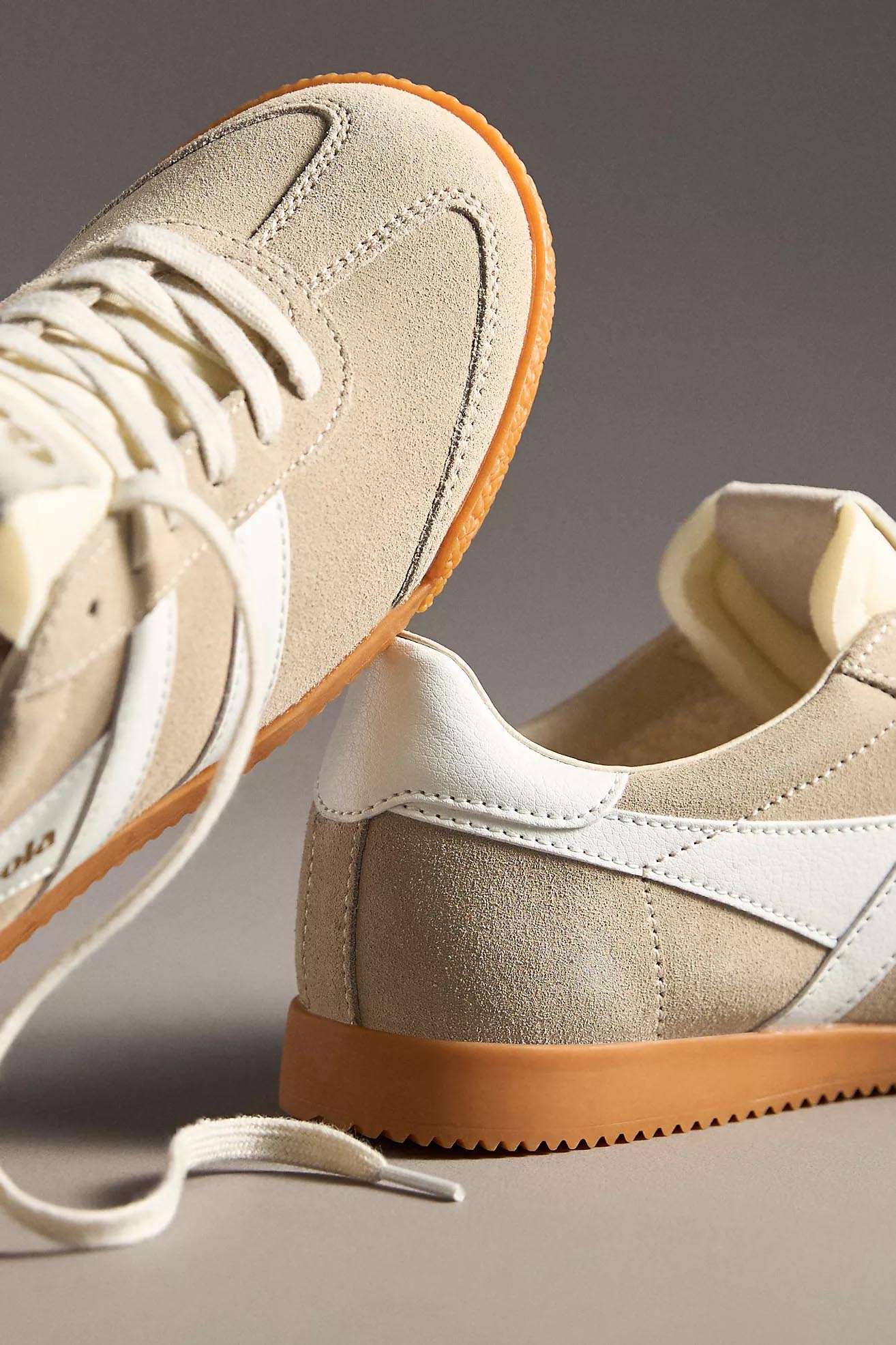 A pair of Gola Elan sneakers in a bone and white colorway, featuring a suede upper with white leather stripes, cream laces, and a gum rubber sole. The "Gola" logo is embossed in gold on the tongue and side.