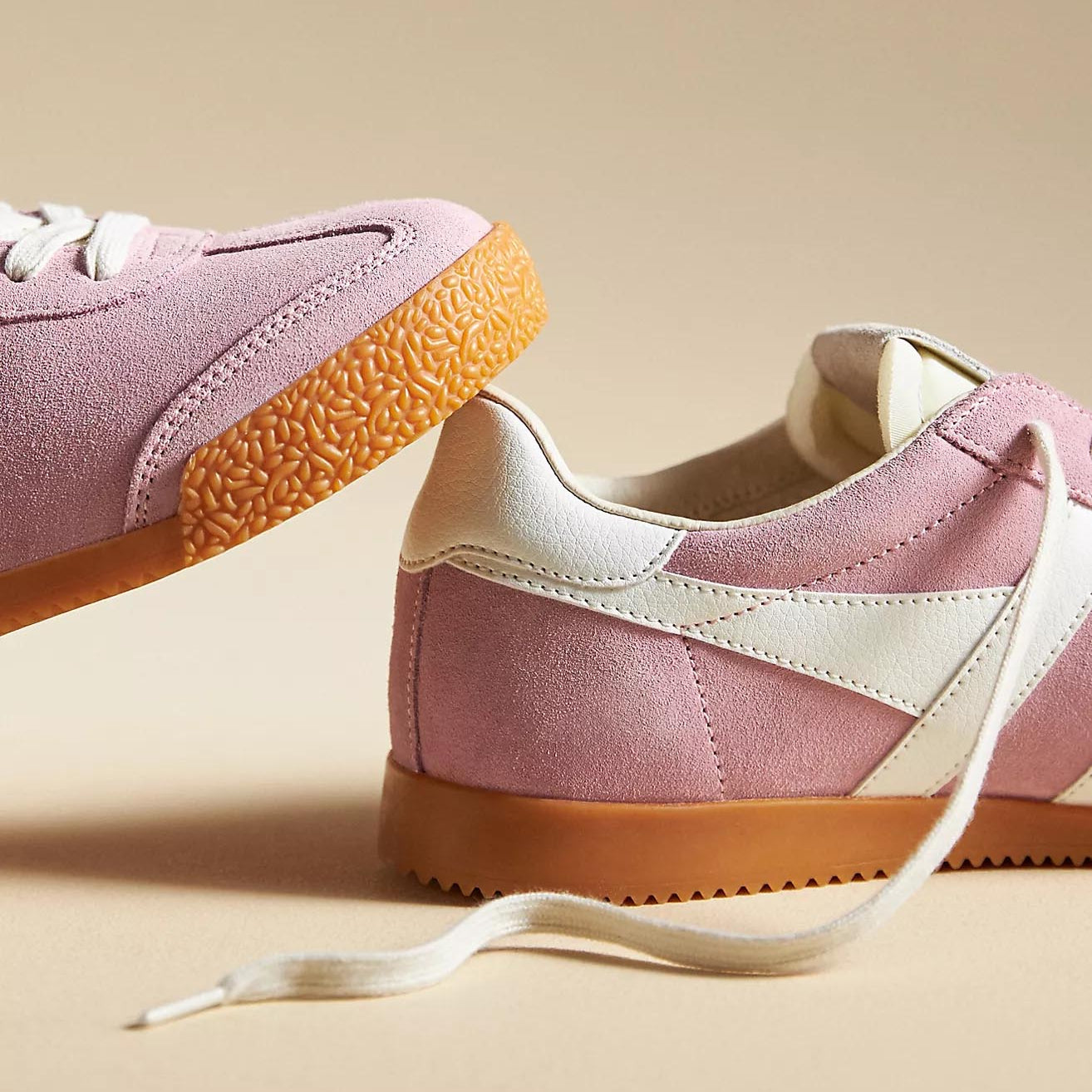 A close-up of the Gola Elan sneakers in Pink Candy & White, featuring a soft pink suede upper, white leather stripes, and a gum rubber sole. The "Gola" logo is embossed in gold on the side, with cream laces adding to the retro aesthetic.