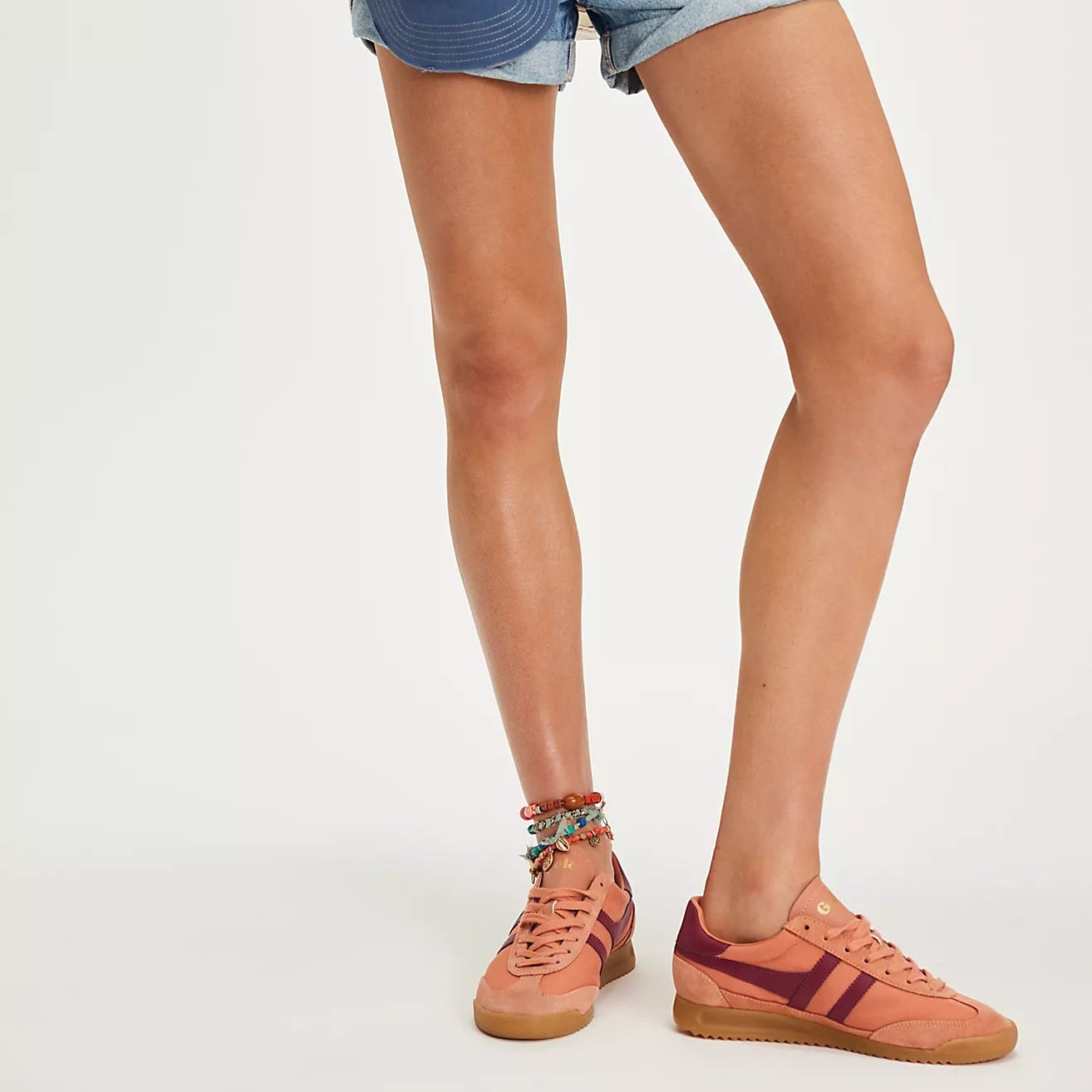Person wearing denim shorts with a colorful patch and pink sneakers on a white background