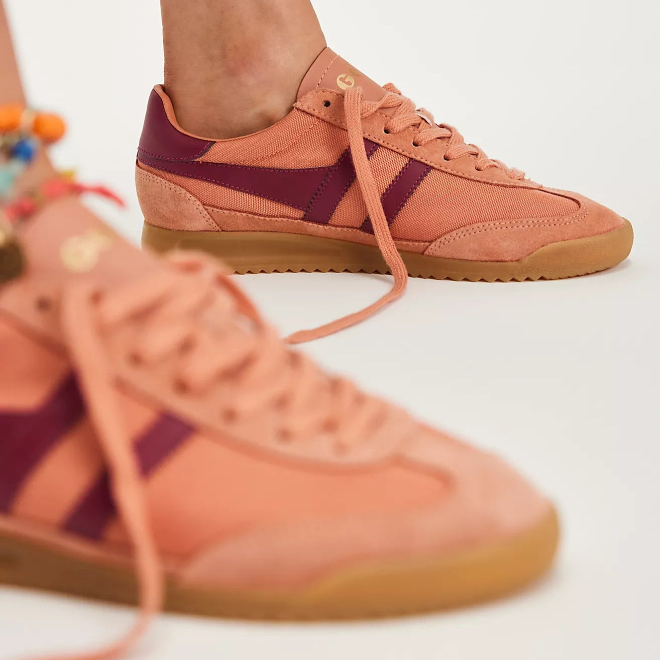 Pair of peach-colored sneakers with purple accents on a white background
