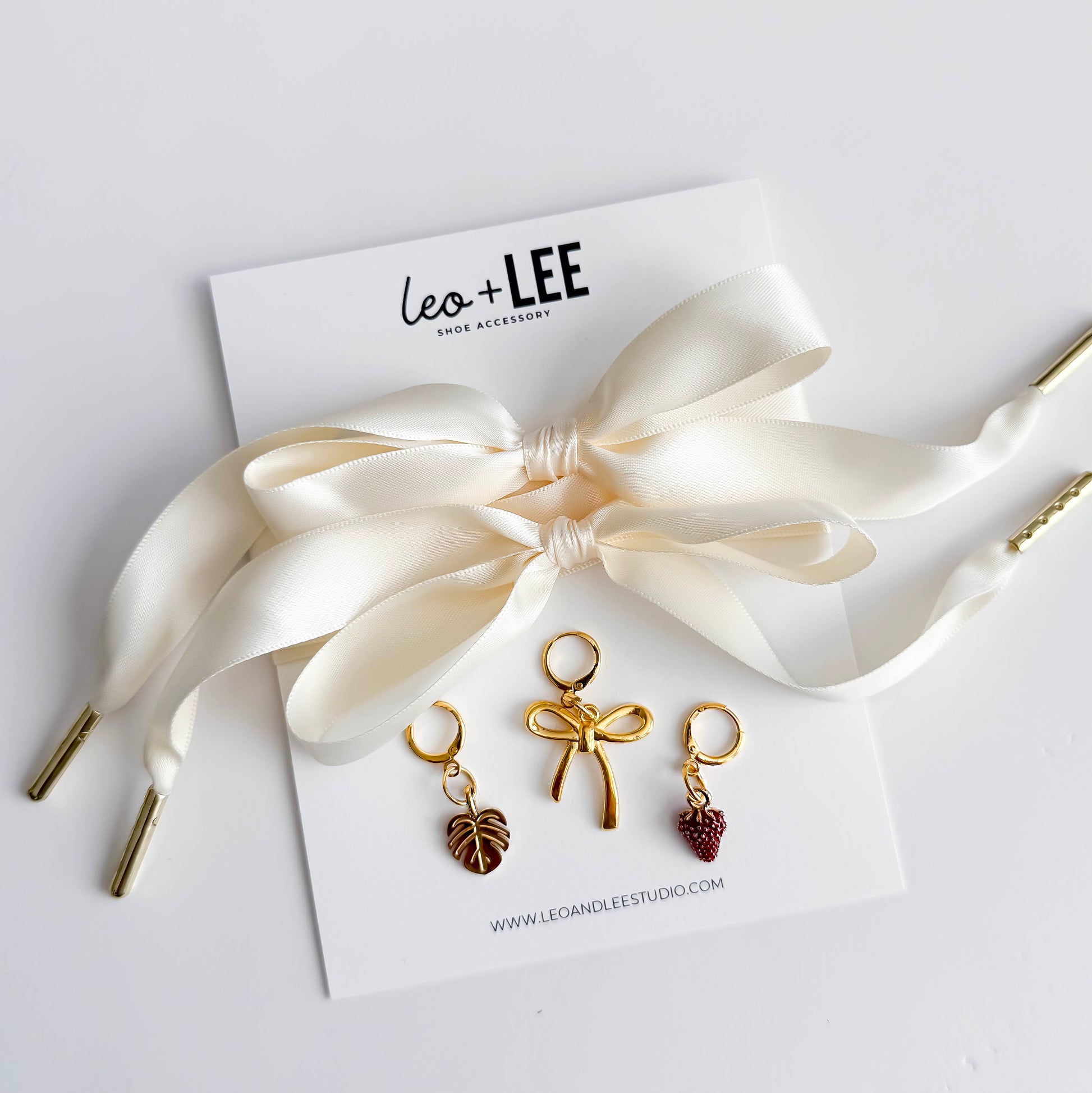 Gold hair accessories with bow and berry charms on a white card with 'leo + LEE' branding.