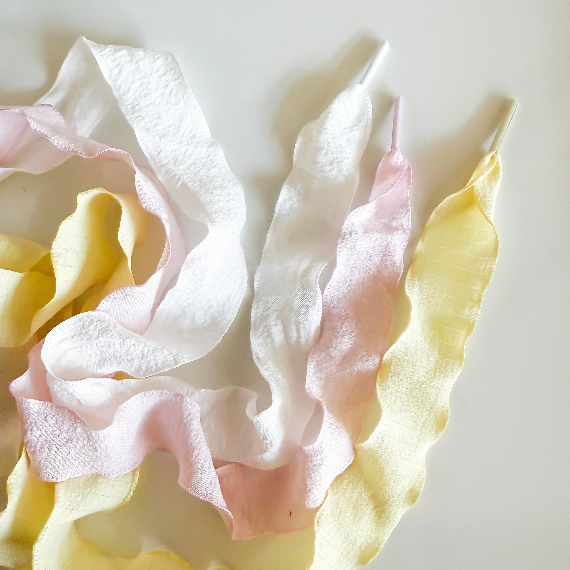 Flat lay of Leo & Lee tennis sneaker charm set with a green tennis ball charm, gold LOVE charm, and gold tennis racquet charm on white ribbon shoelaces.