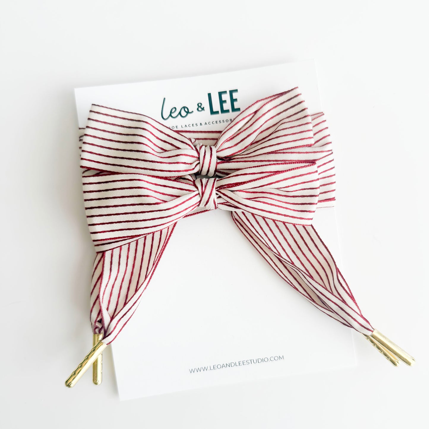Red and white striped hair bow with gold tips on a white background, branded 'Leo & Lee'.