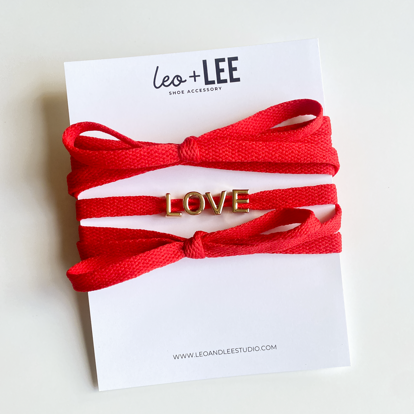 Red and white bow shoelaces with gold 'LOVE' charms from the Leo + Lee Sneaker Charm Set, displayed in packaging and styled individually.