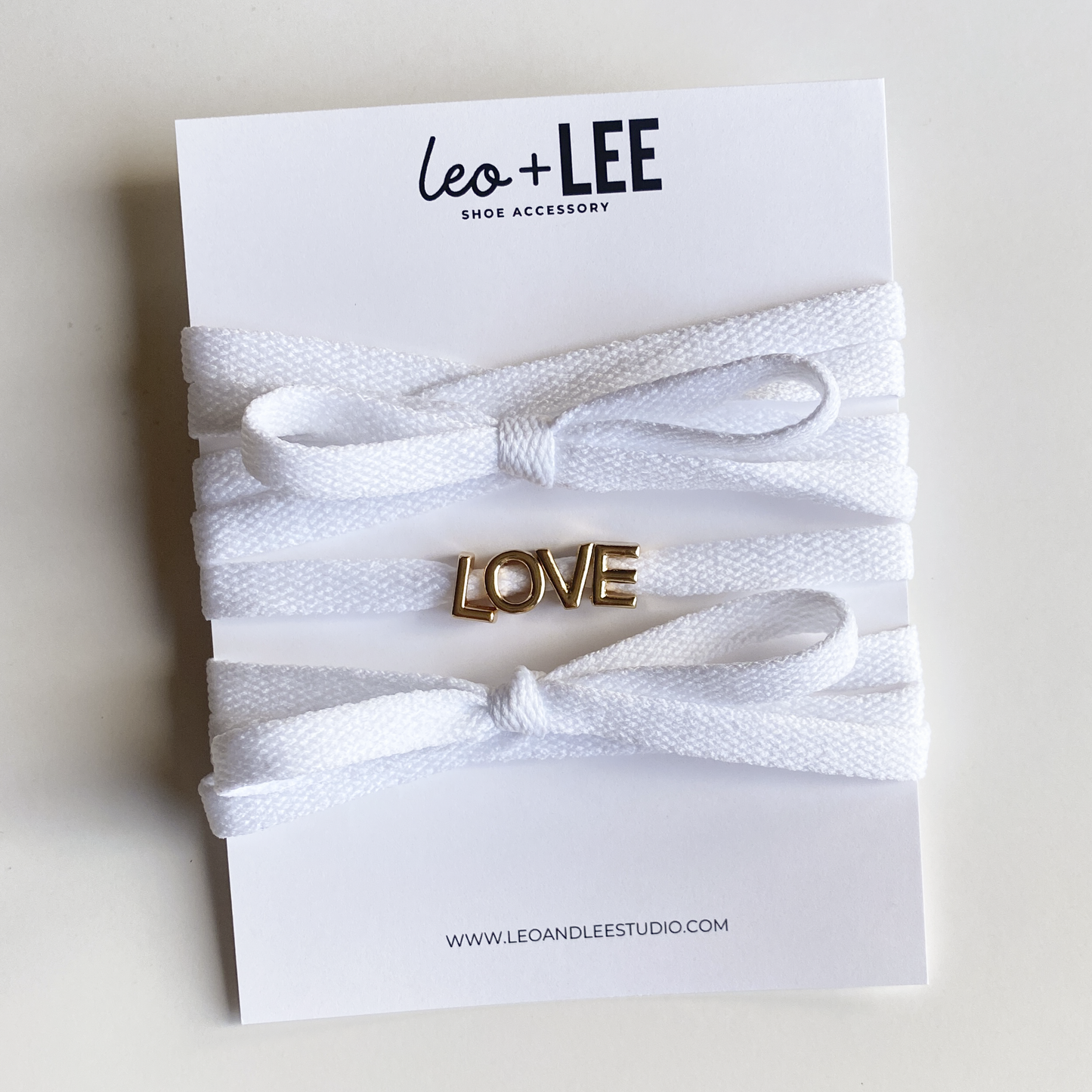 Red and white bow shoelaces with gold 'LOVE' charms from the Leo + Lee Sneaker Charm Set, displayed in packaging and styled individually.