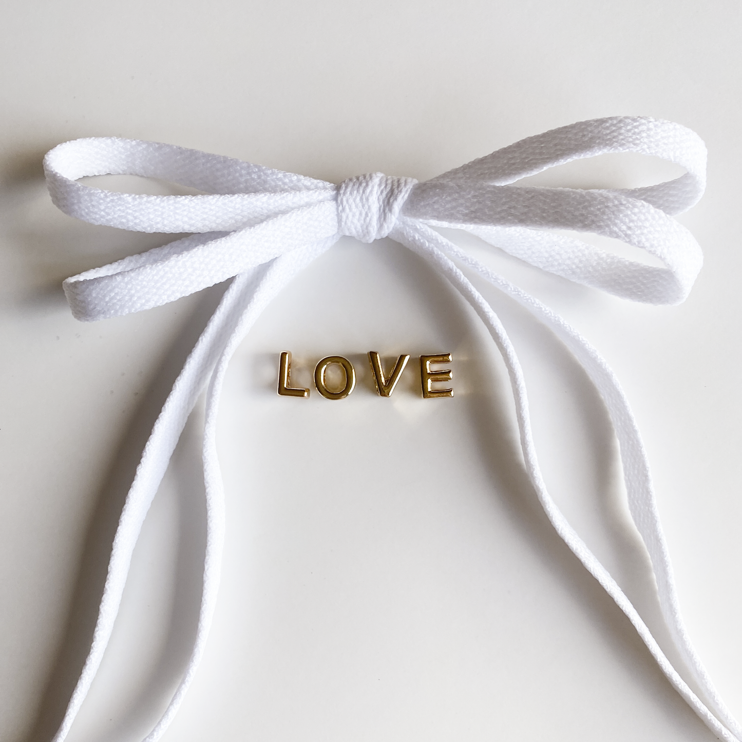 Red and white bow shoelaces with gold 'LOVE' charms from the Leo + Lee Sneaker Charm Set, displayed in packaging and styled individually.