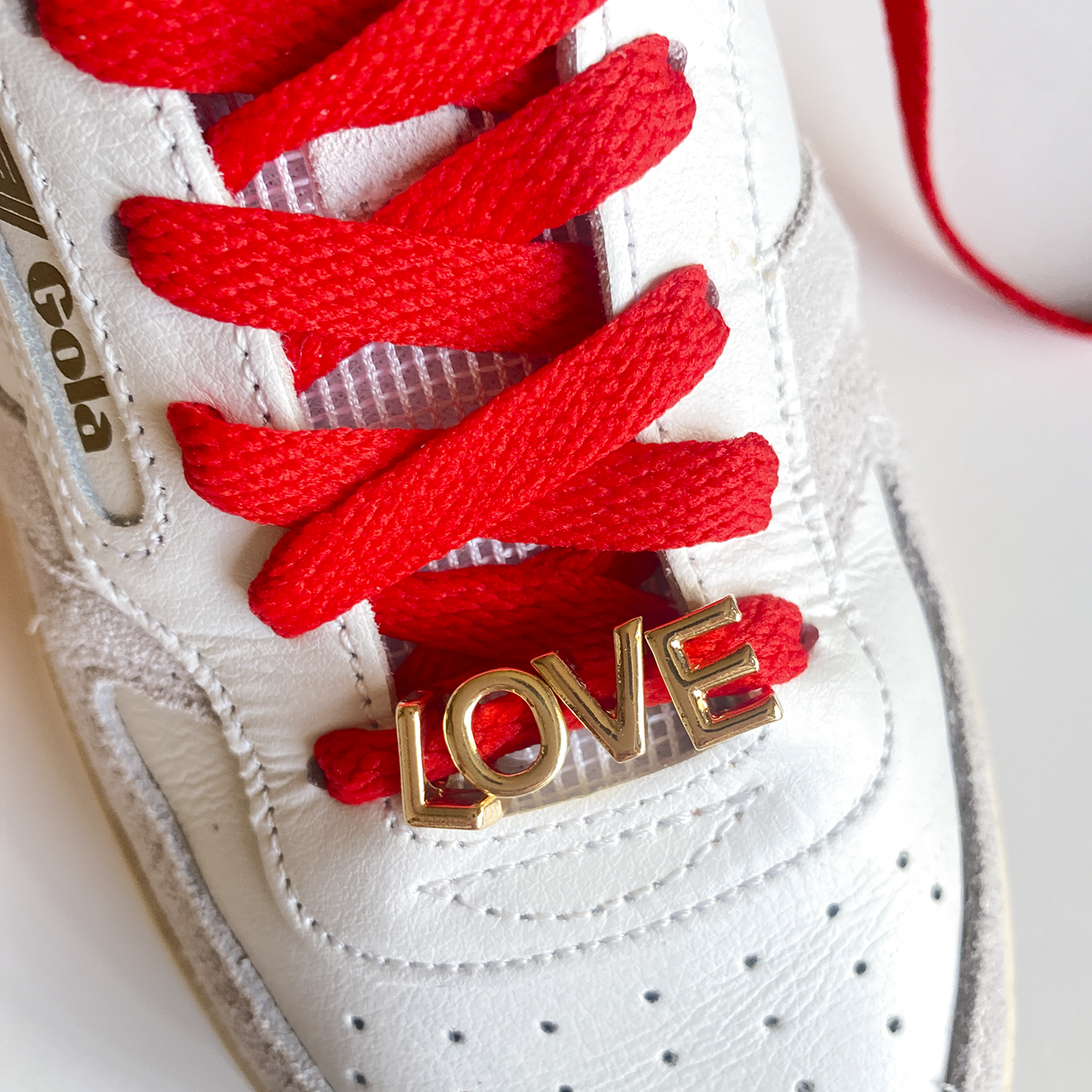 Red and white bow shoelaces with gold 'LOVE' charms from the Leo + Lee Sneaker Charm Set, displayed in packaging and styled individually.