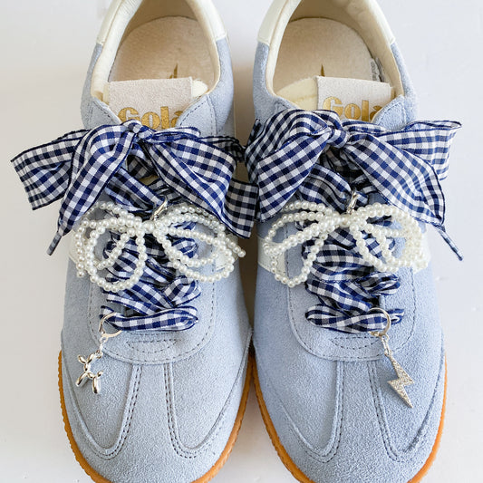 A set of navy gingham ribbon shoe laces and pearl strand laces displayed on a Leo + Lee card, featuring two silver charms — a balloon dog and a rhinestone lightning bolt — arranged neatly on a white background.