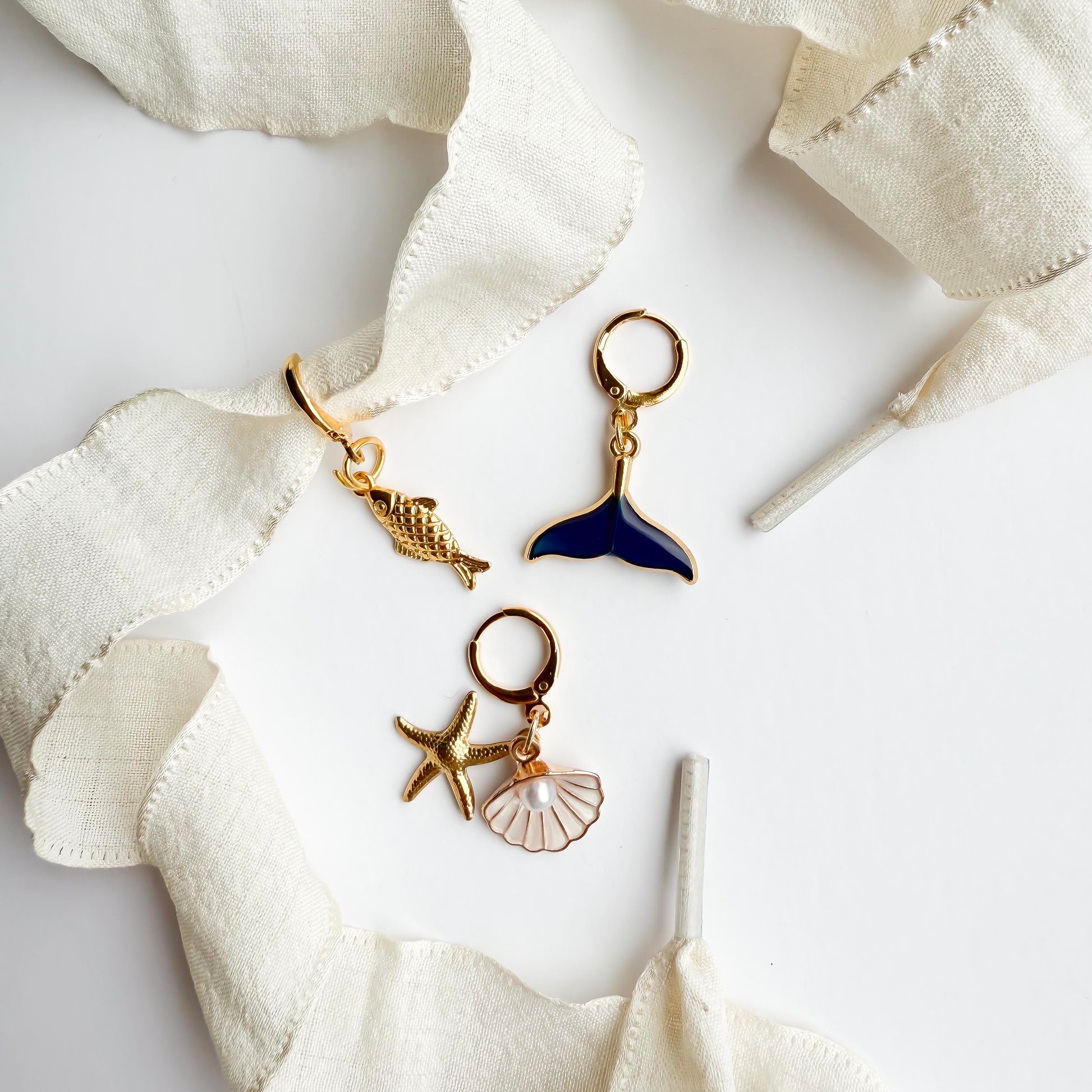 Beige sneaker with white satin laces featuring gold ocean-themed shoelace charms including a whale tail, starfish, seashell, and conch shell, styled flat on a white background.