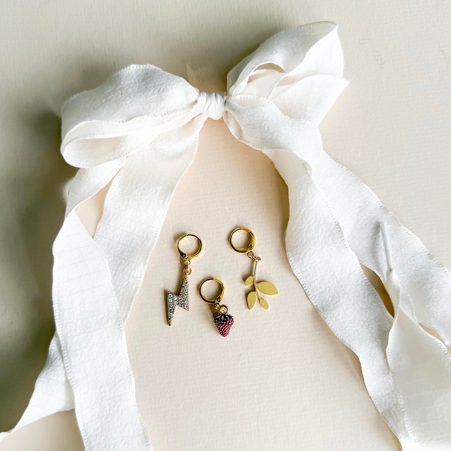 White ribbon shoelaces with gold sneaker charms – lightning bolt, leaf, and strawberry – displayed on product card by Leo + Lee Studio