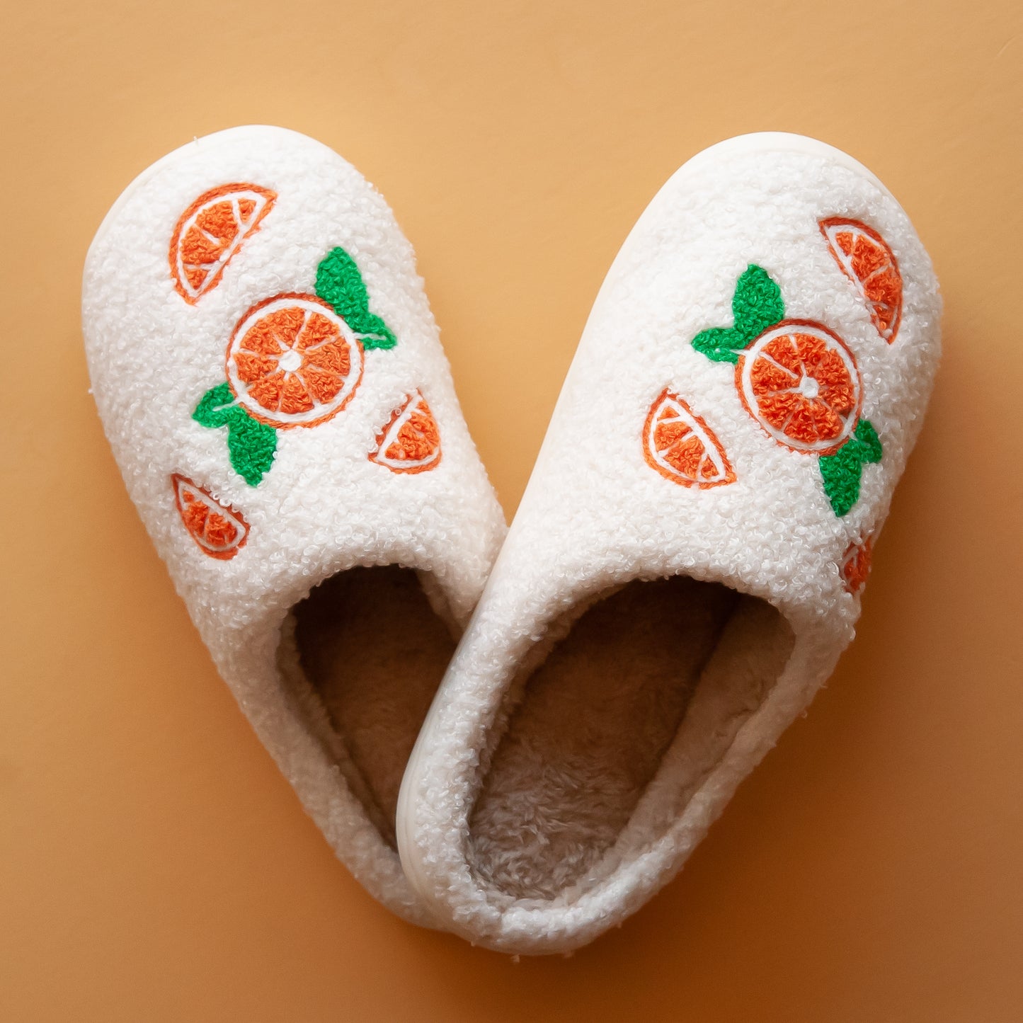 Pair of cozy slippers with custom designed oranges on each slipper, featuring a soft, plush exterior and a fluffy interior lining for maximum comfor