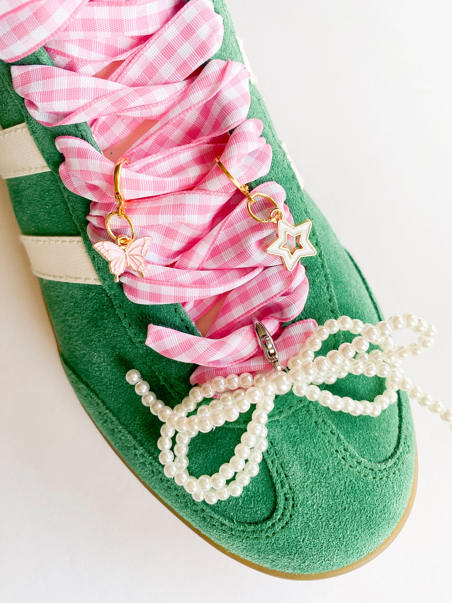 Gold shoe charms with pink butterfly and white star designs, displayed with pink gingham ribbon shoelaces and pearl bead shoelaces on white background.