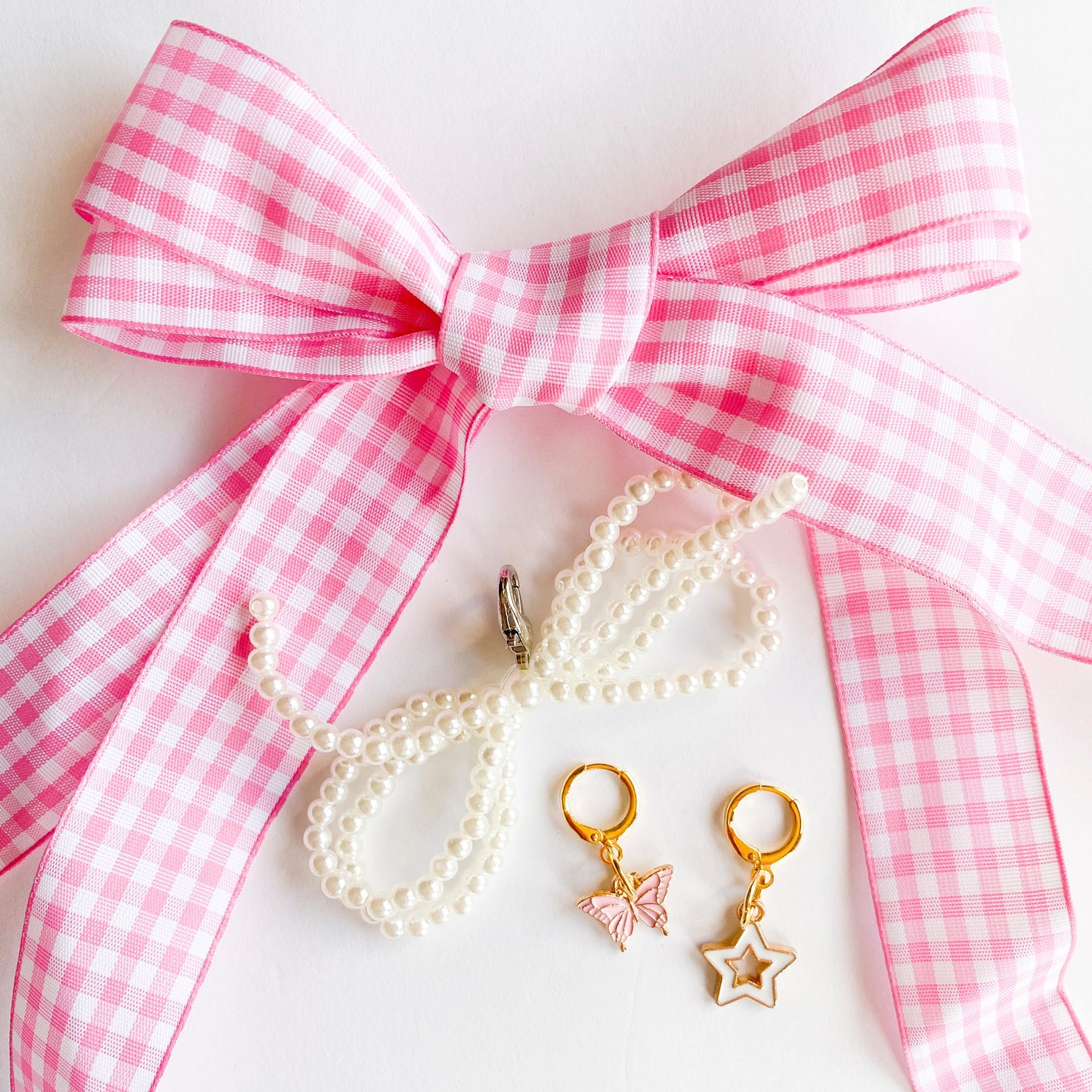 Gold shoe charms with pink butterfly and white star designs, displayed with pink gingham ribbon shoelaces and pearl bead shoelaces on white background.