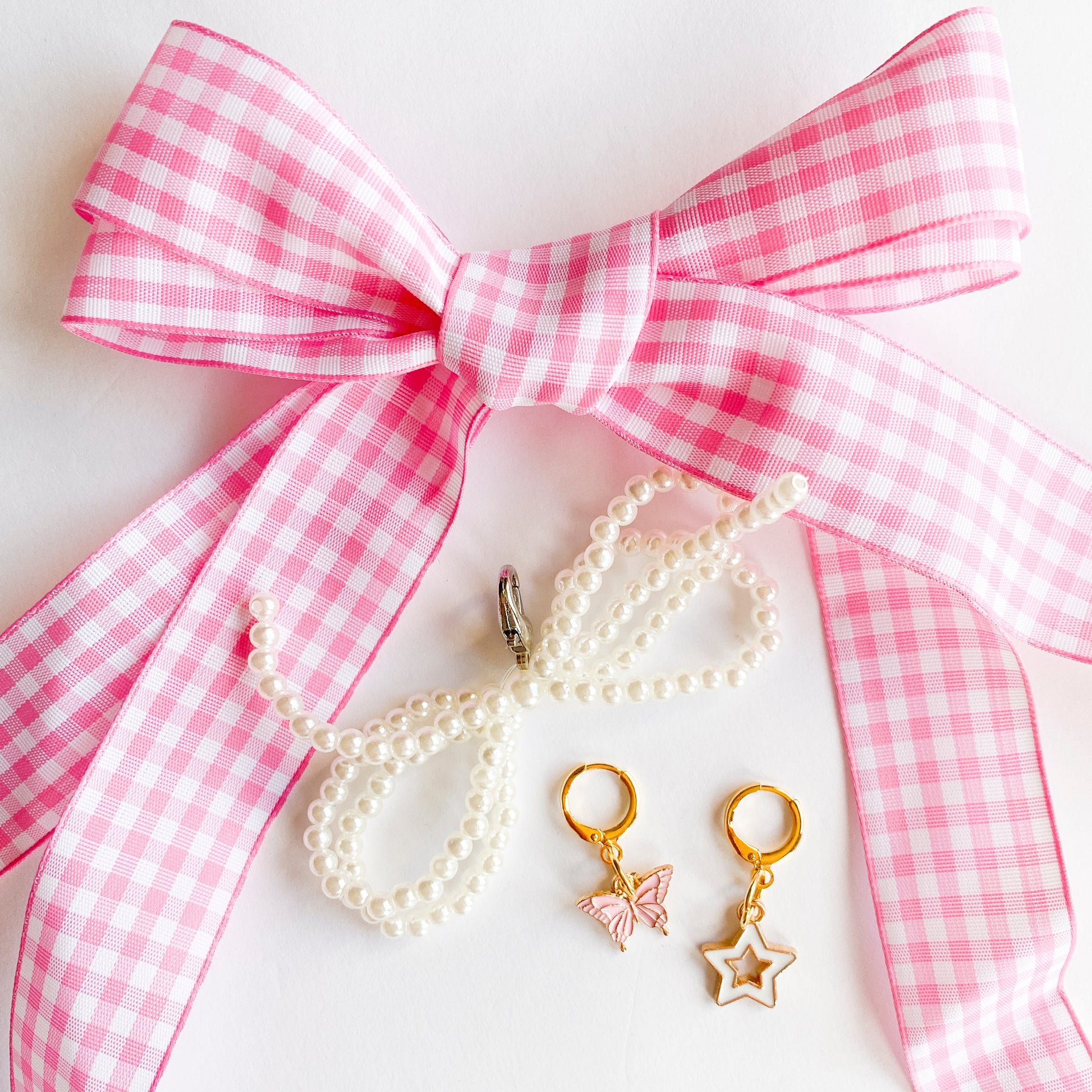 Gold shoe charms with pink butterfly and white star designs, displayed with pink gingham ribbon shoelaces and pearl bead shoelaces on white background.
