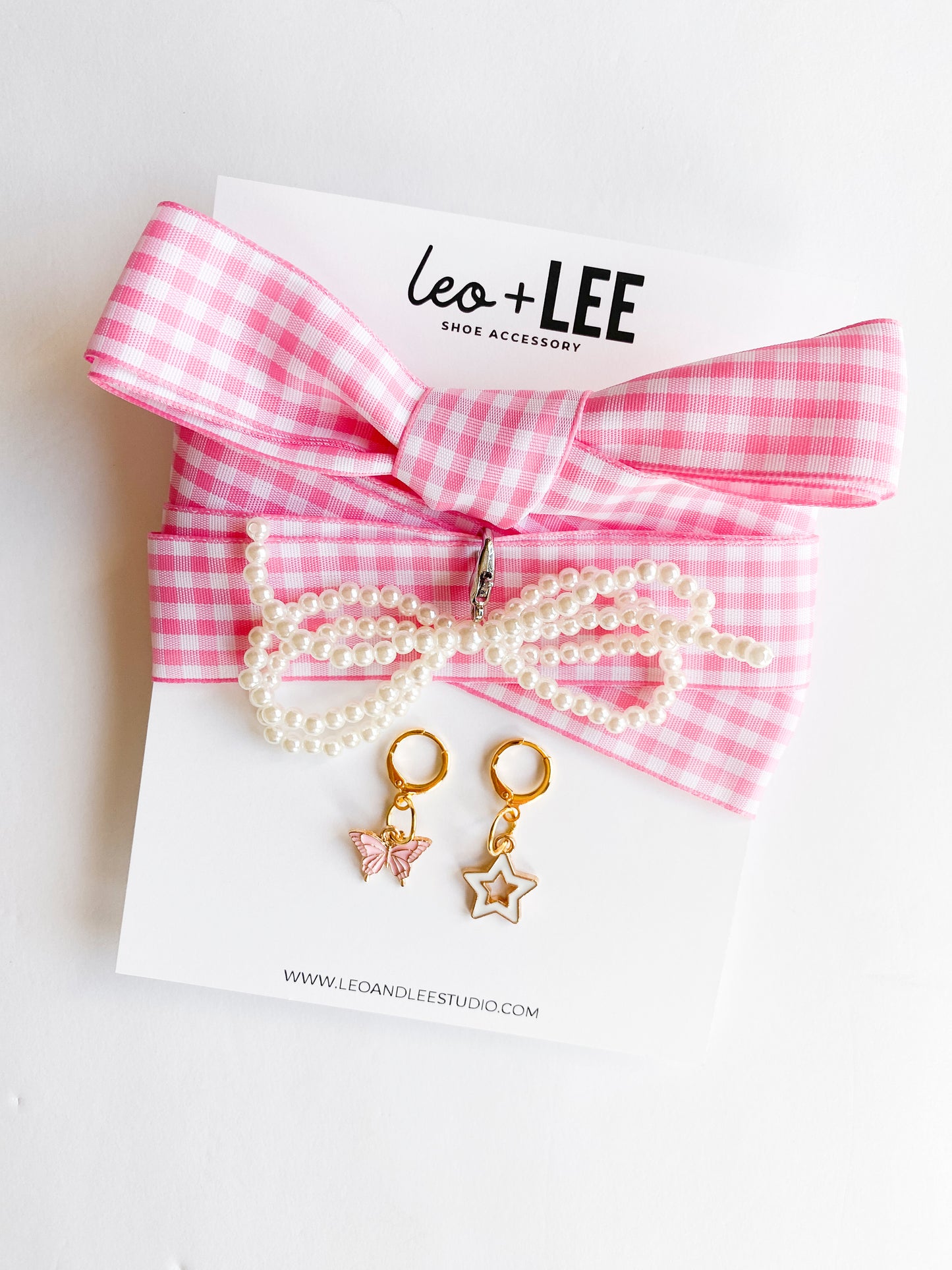 Gold shoe charms with pink butterfly and white star designs, displayed with pink gingham ribbon shoelaces and pearl bead shoelaces on white background.