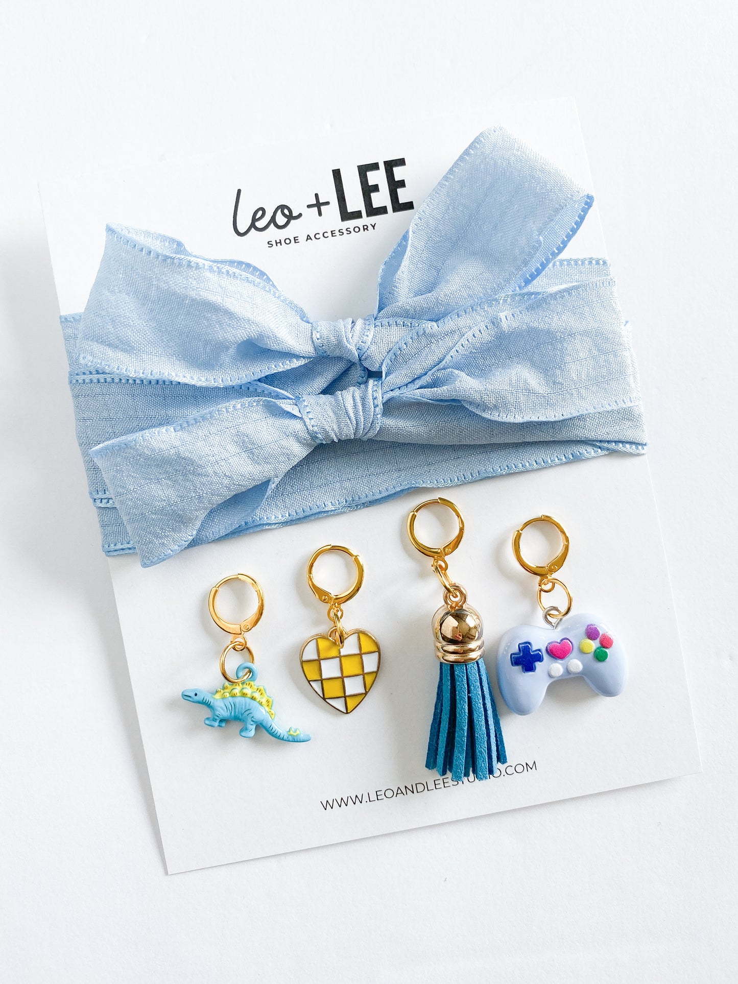 Assorted kids sneaker charm sets displayed in rows, each featuring 100cm bow-style ribbon shoelaces and four colorful enamel shoe charms on branded cards.