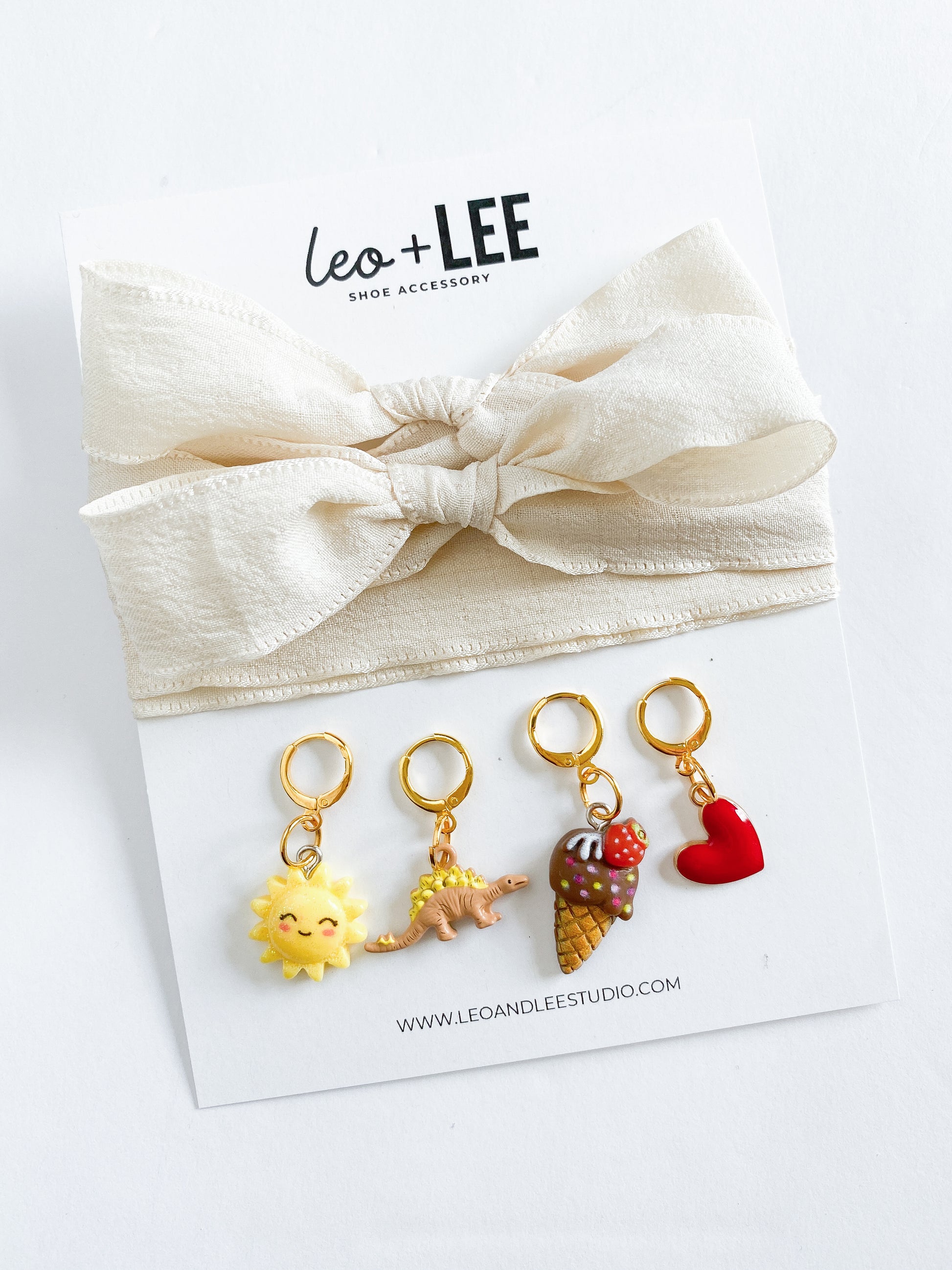 Assorted kids sneaker charm sets displayed in rows, each featuring 100cm bow-style ribbon shoelaces and four colorful enamel shoe charms on branded cards.