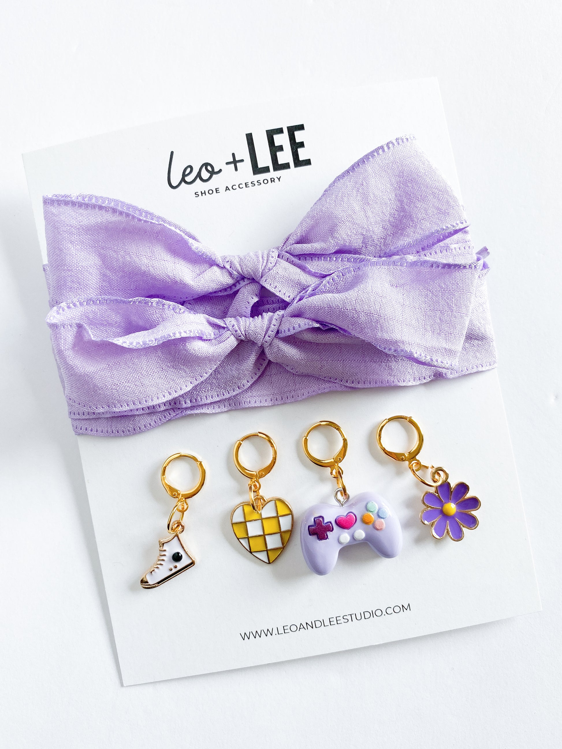 Assorted kids sneaker charm sets displayed in rows, each featuring 100cm bow-style ribbon shoelaces and four colorful enamel shoe charms on branded cards.