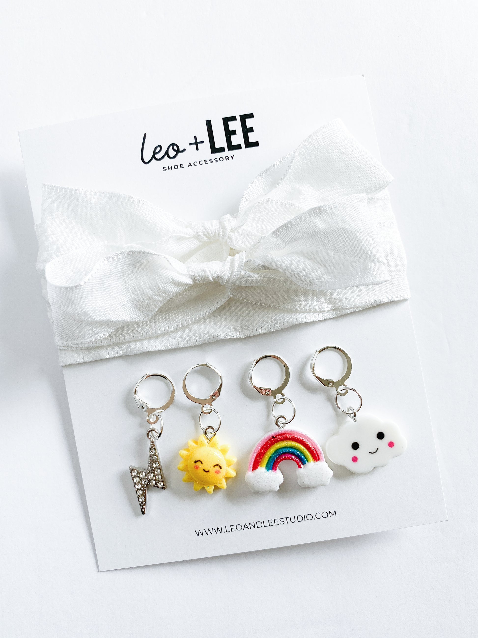 Assorted kids sneaker charm sets displayed in rows, each featuring 100cm bow-style ribbon shoelaces and four colorful enamel shoe charms on branded cards.