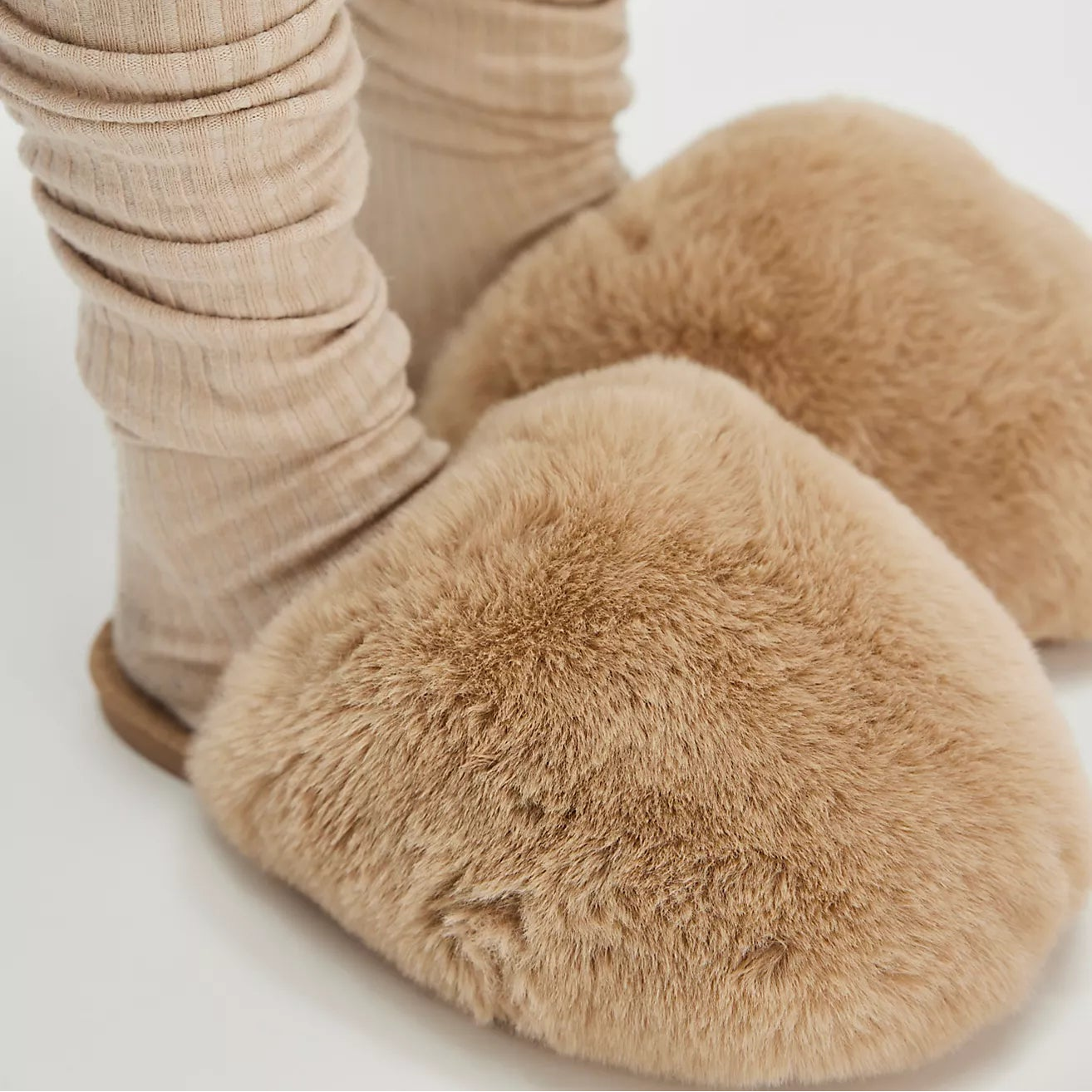 Beige slippers worn with beige socks on a white background