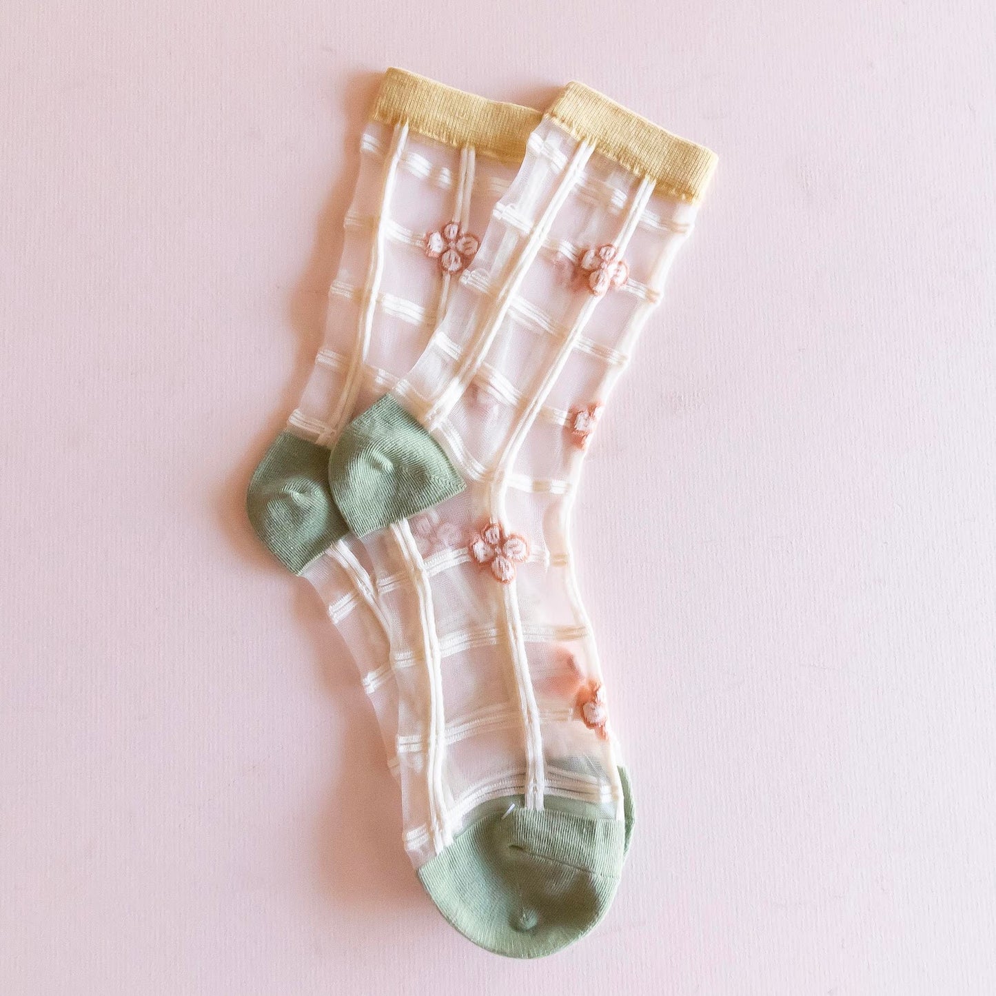 Pair of sheer socks with floral patterns and green toes on a light pink background