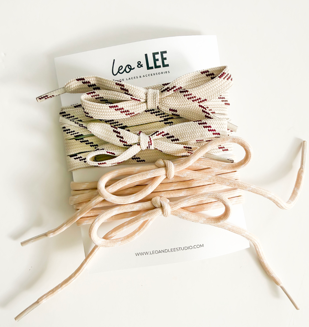 A stack of woven shoelaces from Leo & Lee, featuring a cream and burgundy plaid pattern on top and solid beige underneath, presented on a white backing card.