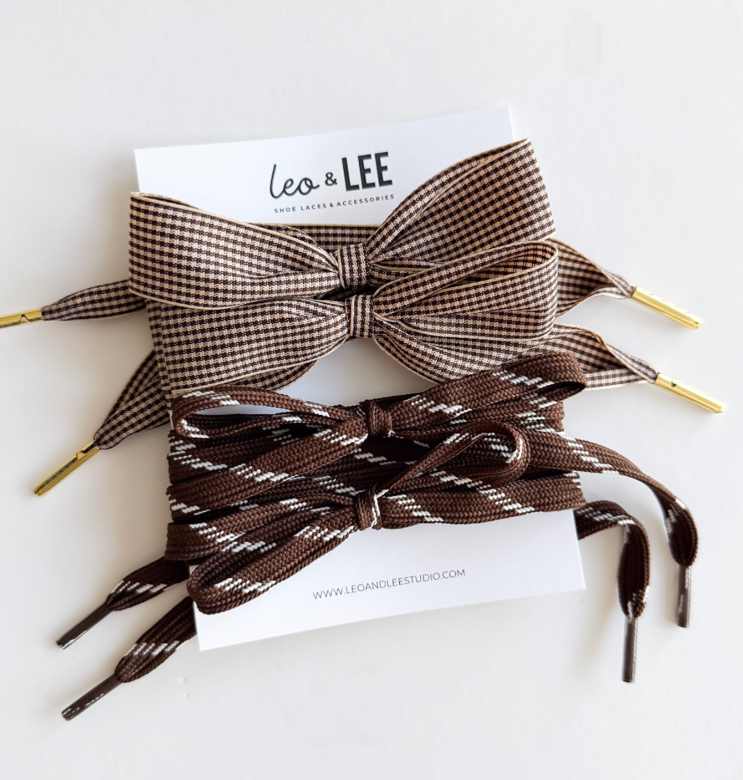 Two brown patterned shoelaces with gold metal tips and a matching brown bow, displayed on a white backing card with the brand name Leo & Lee.