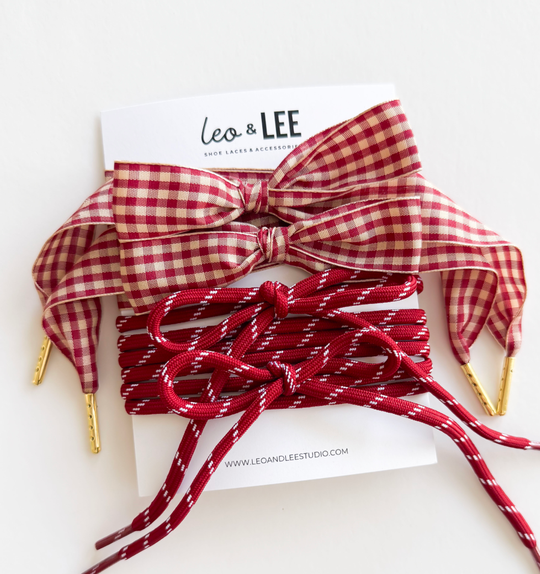 A pair of red and white gingham ribbon shoelaces with gold metal tips, shown tied in a bow and wrapped around a red cord, displayed on a white backing card with the brand name 'leo & LEE'.