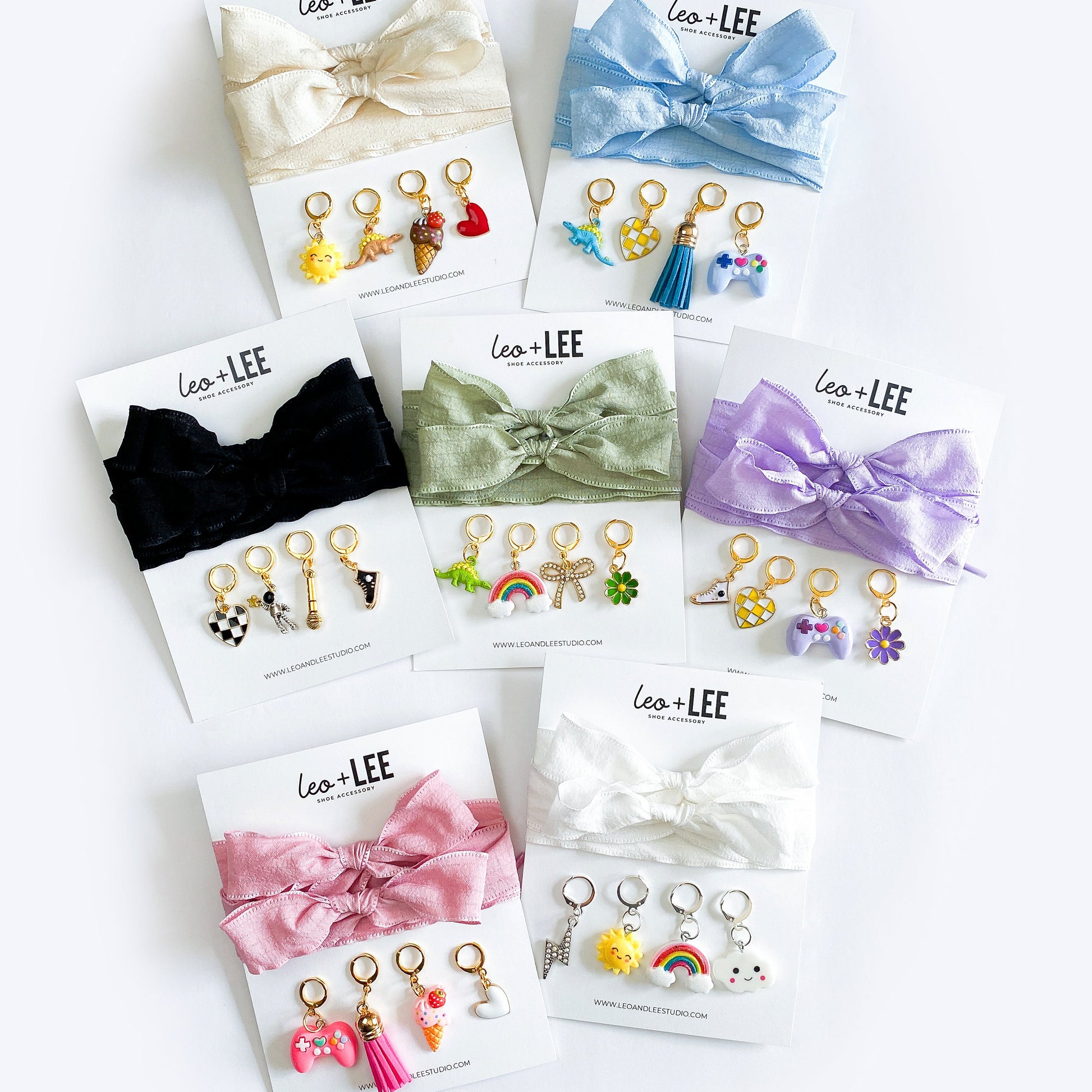 Assorted kids sneaker charm sets displayed in rows, each featuring 100cm bow-style ribbon shoelaces and four colorful enamel shoe charms on branded cards.