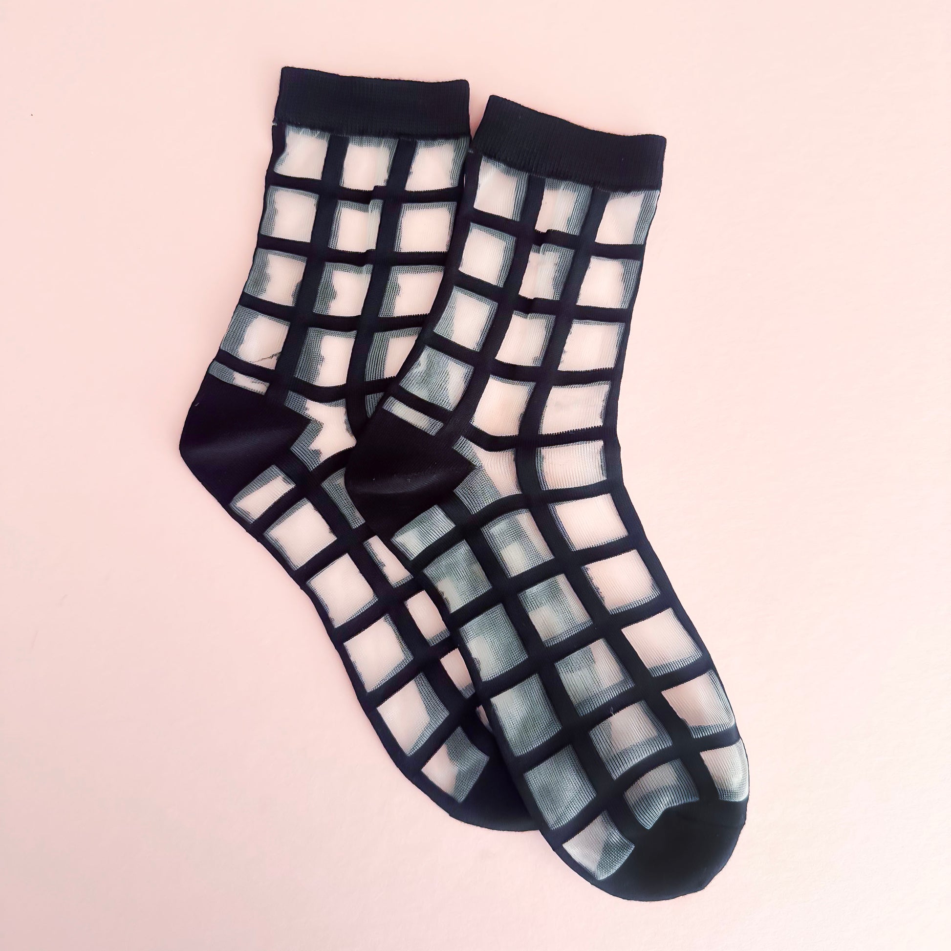 Sheer black and white grid patterned socks on a light pink background
