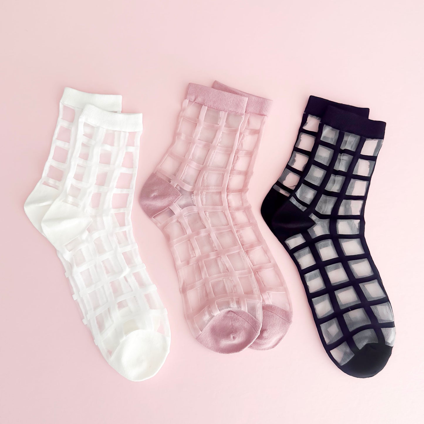 Three pairs of sheer grid-patterned socks on a pink background