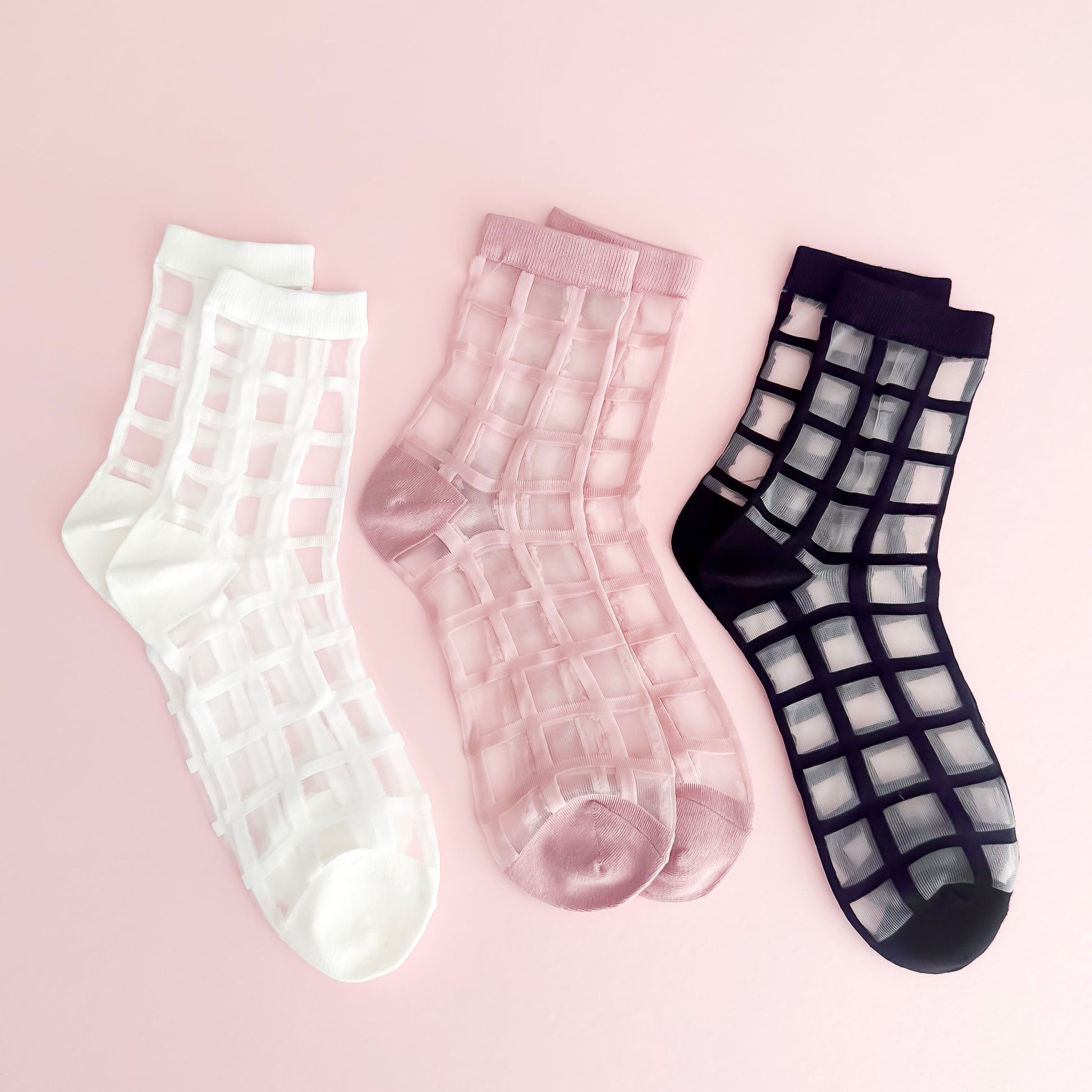 Three pairs of sheer grid-patterned socks on a pink background
