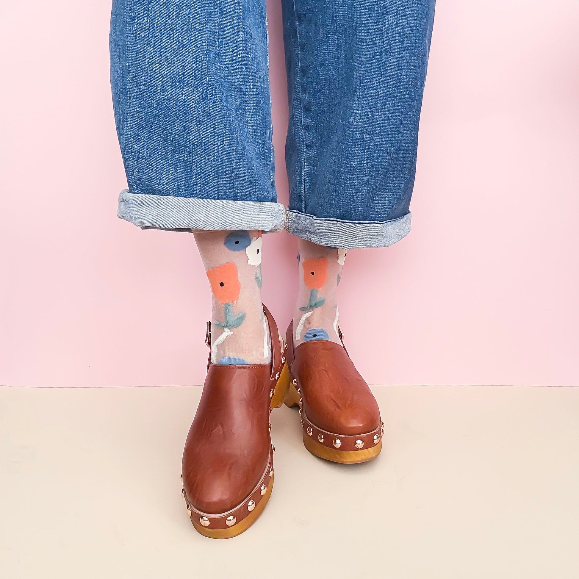 Person wearing brown clogs with colorful socks featuring cartoon-like designs on a light pink background.