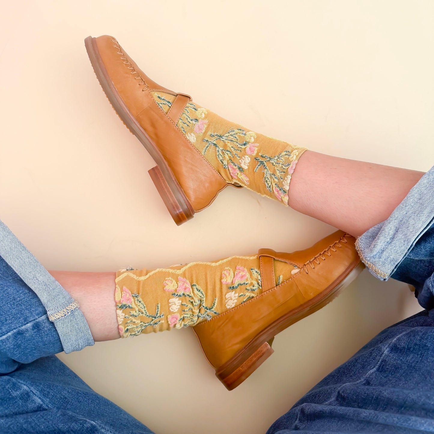 Brown leather shoes with floral embroidery on mustard yellow socks against a beige background