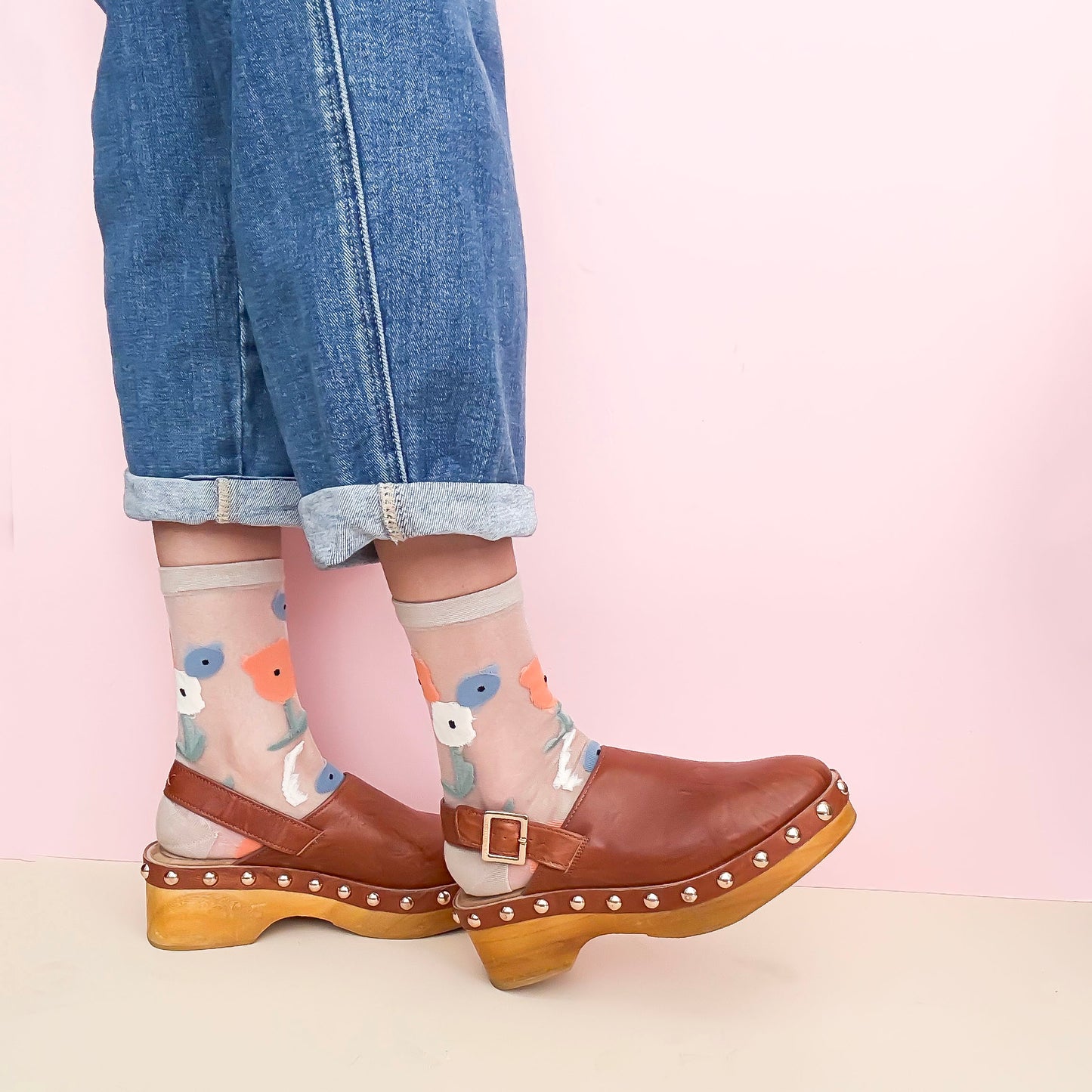Person wearing brown clogs with wooden soles on a light pink background