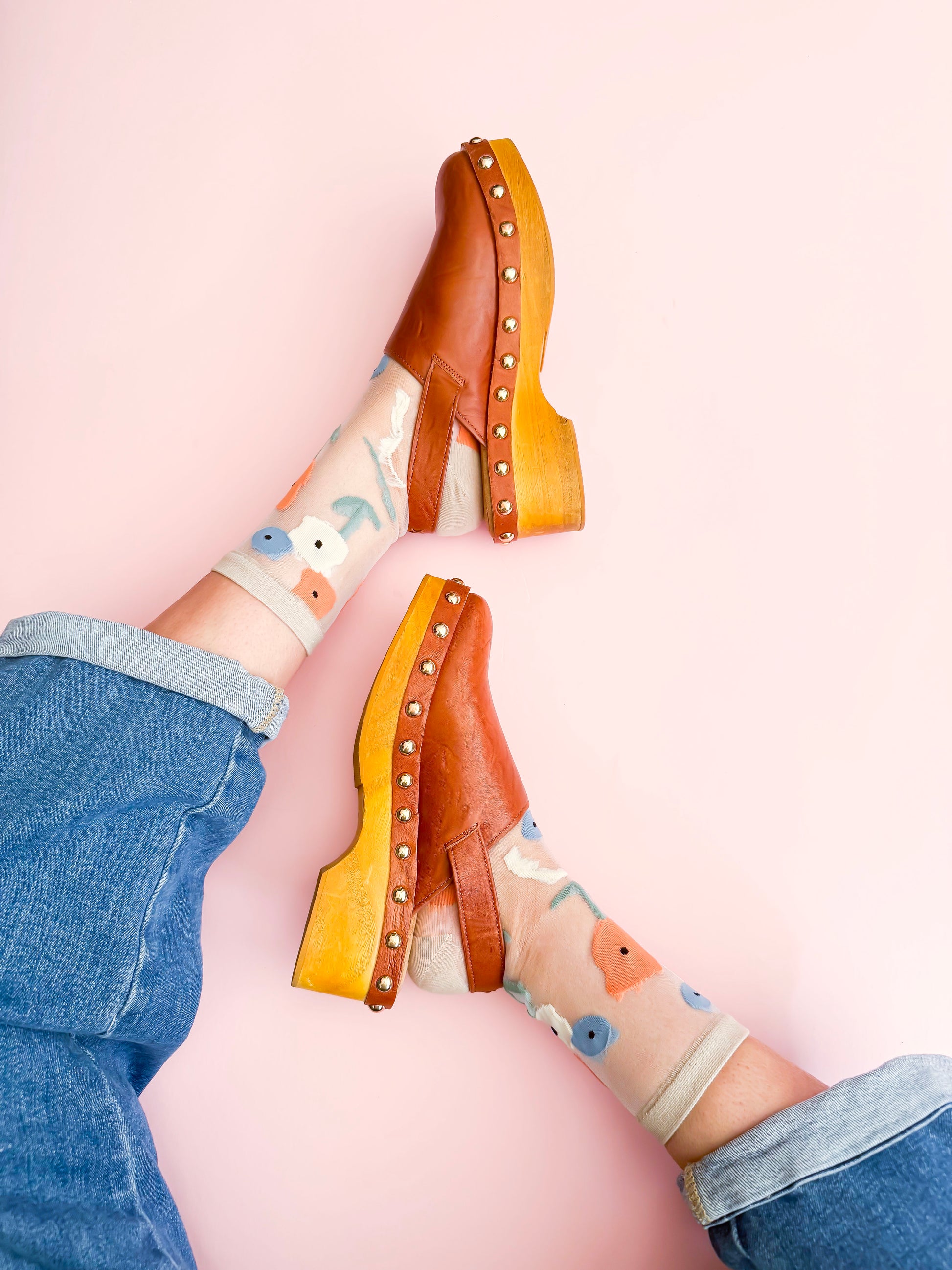 Clogs with studded details worn with patterned socks on a pink background