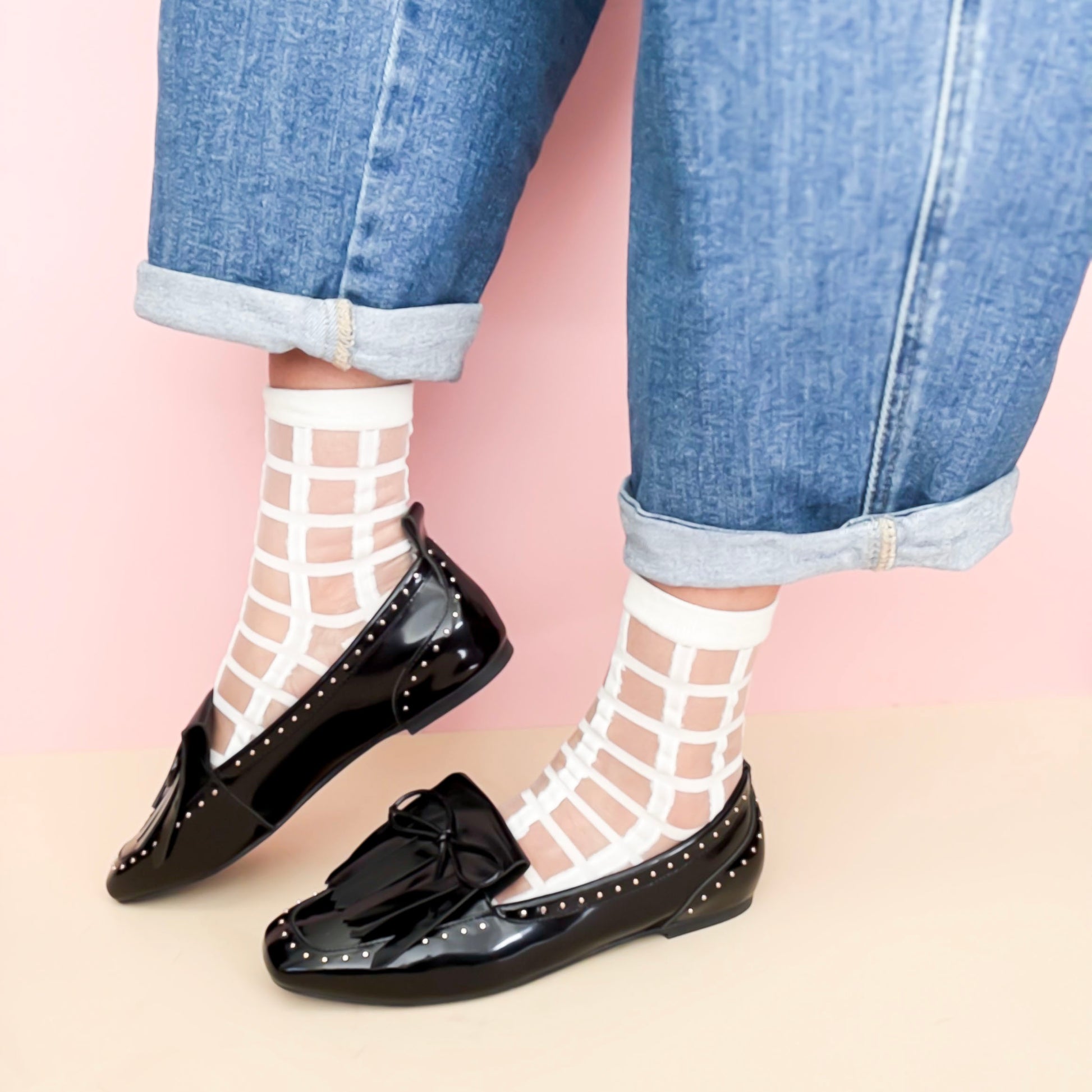 Black loafers worn with white fishnet socks and blue jeans on a pink background