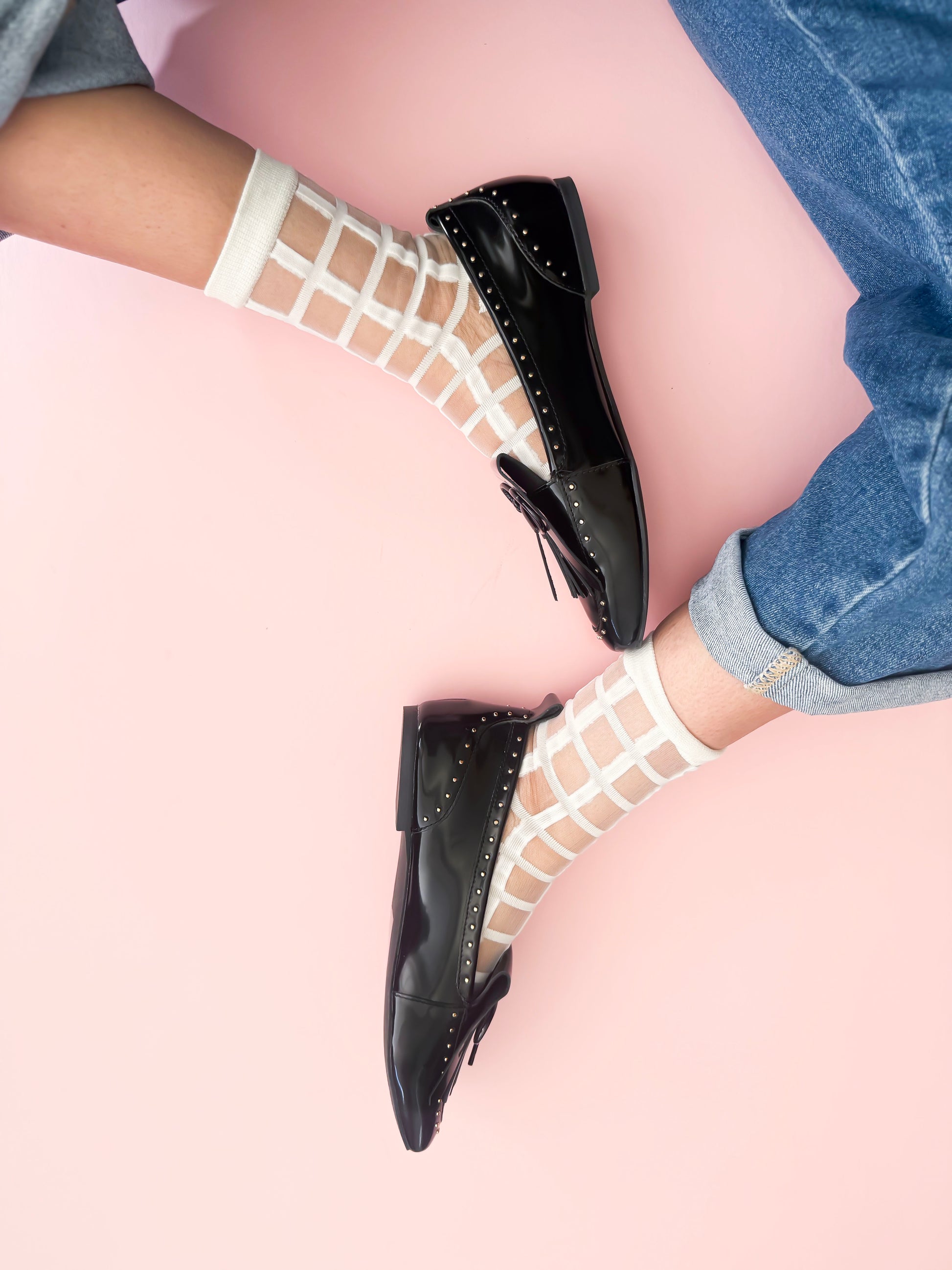 Black shoes worn with white fishnet stockings on a light pink surface