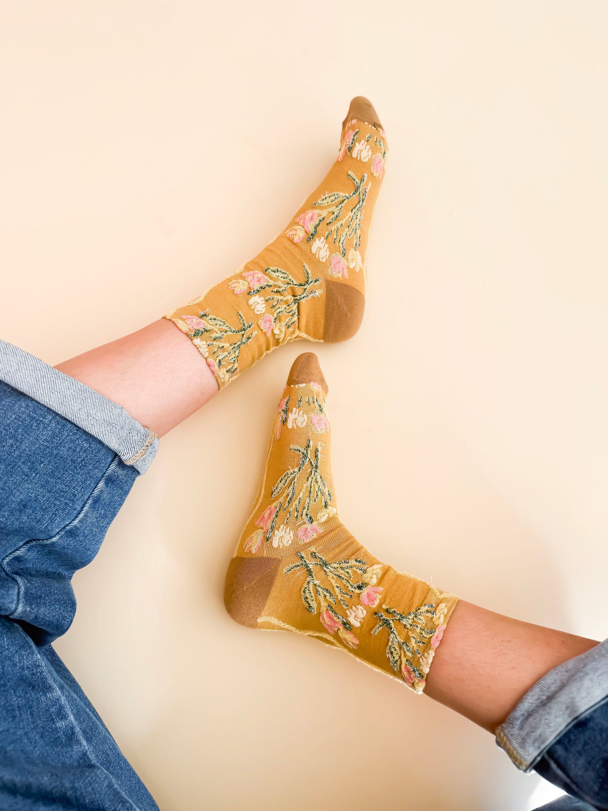 Mustard yellow socks with floral pattern worn by a person on a beige background