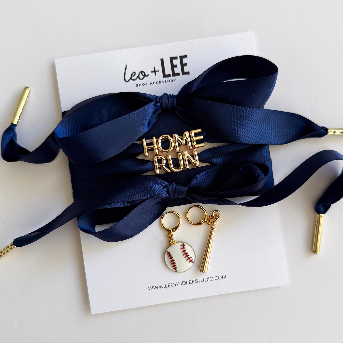 Navy blue ribbon with gold 'HOMERUN' brooch and key-shaped charms on a white card with 'Leo + Lee' branding.